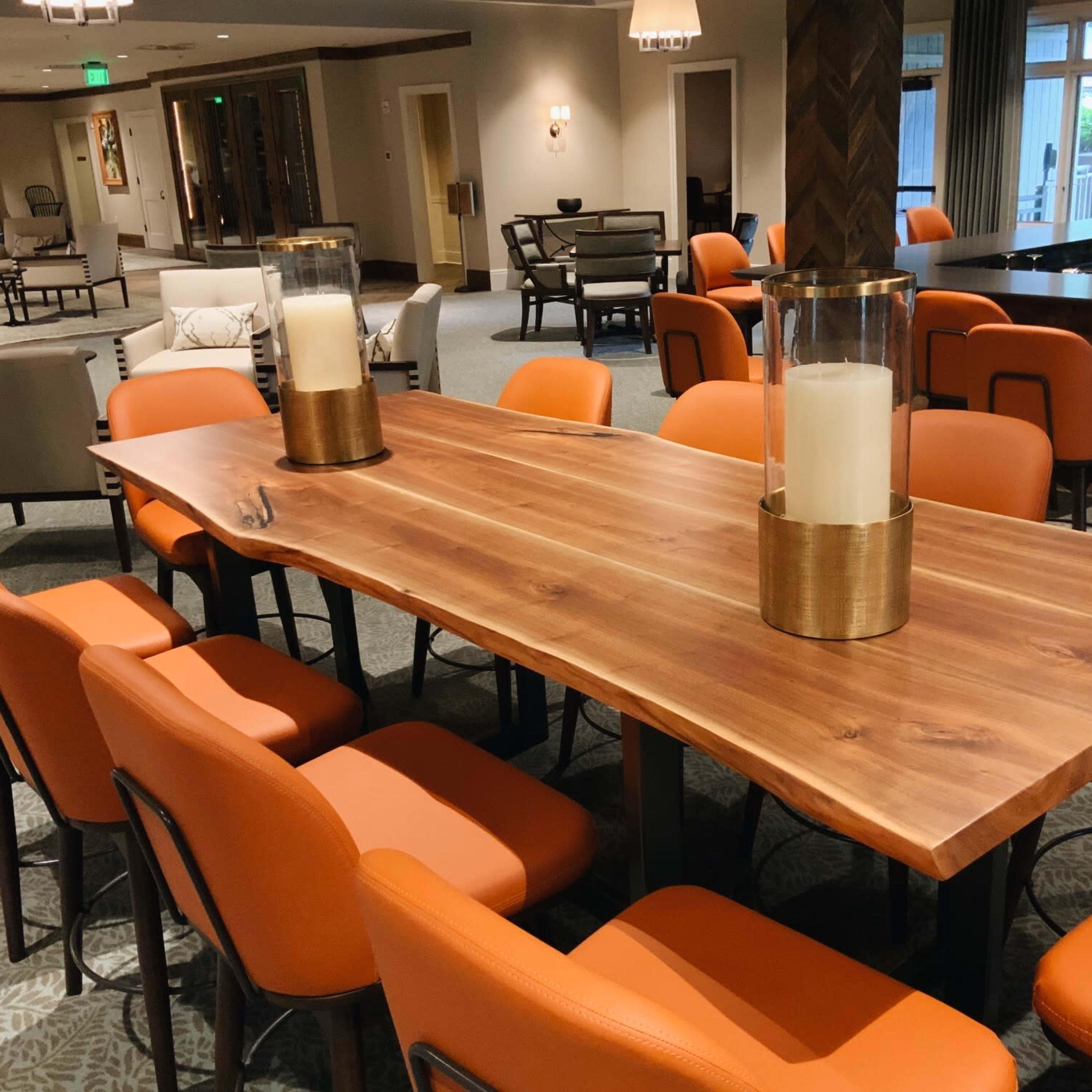 A long wooden table with two glass candle holders is surrounded by orange chairs in a spacious dining area.