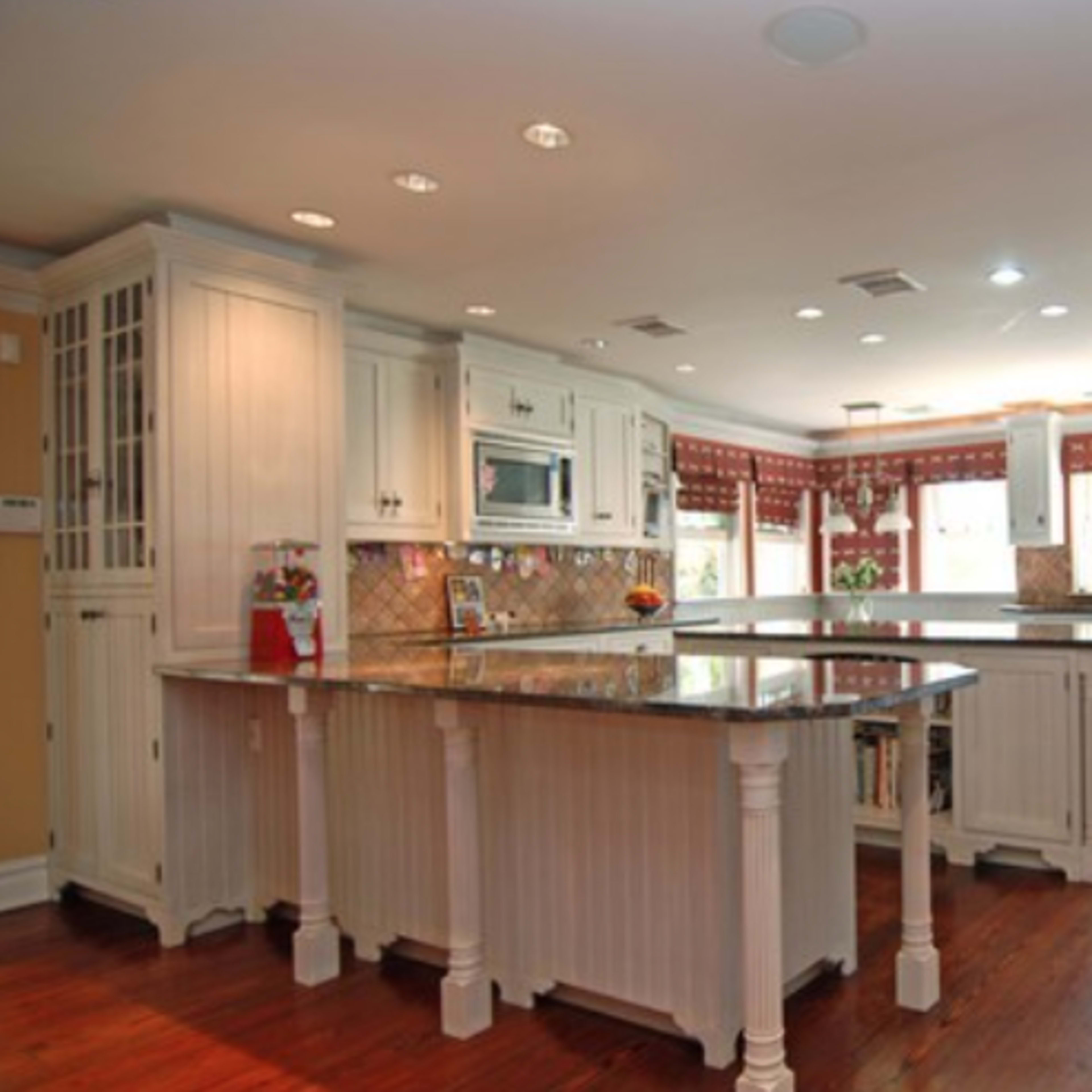 The kitchen features white cabinetry, a central island with marble countertops, and large windows offering natural light.