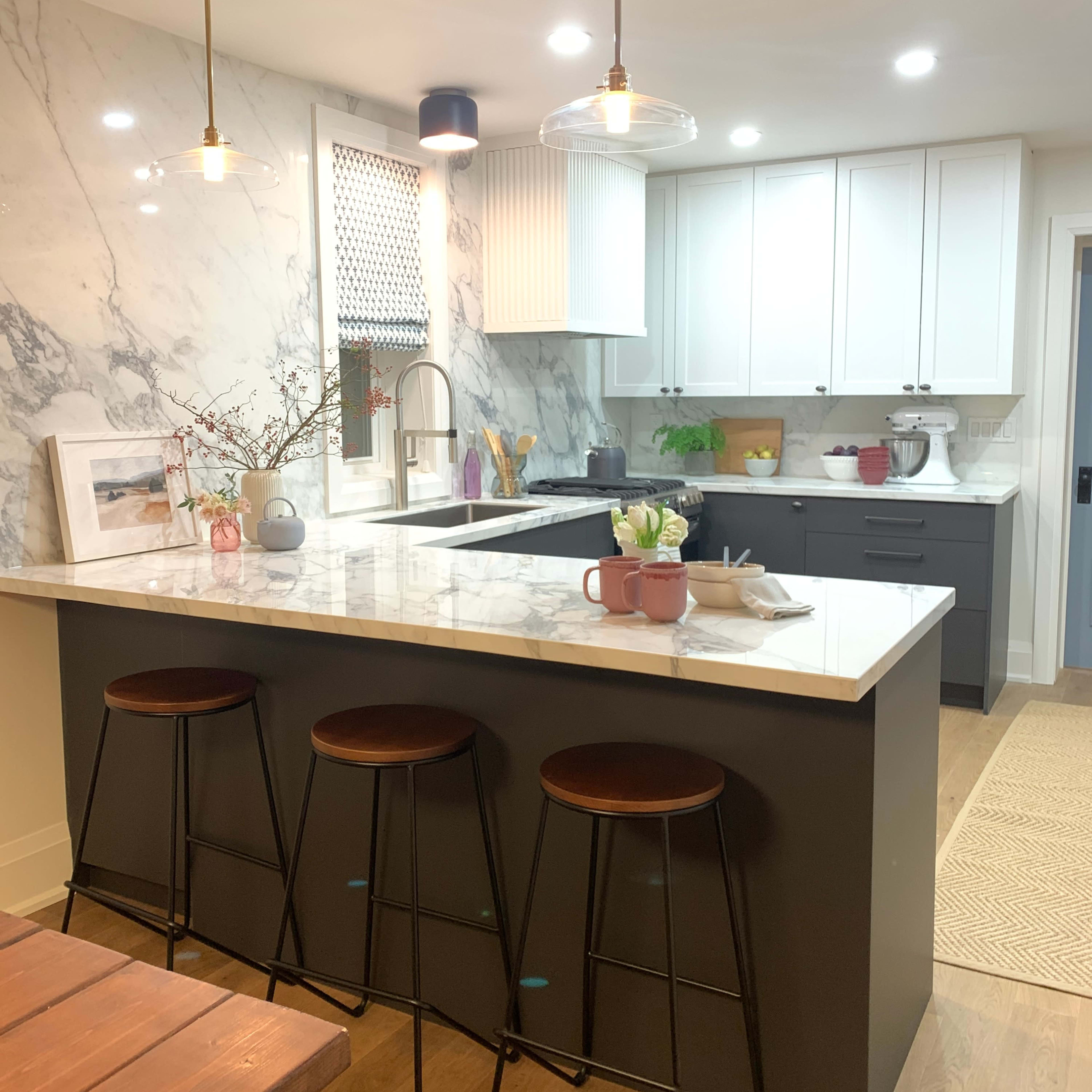 A modern kitchen features a marble backsplash, white cabinets, and a dark island with three bar stools.