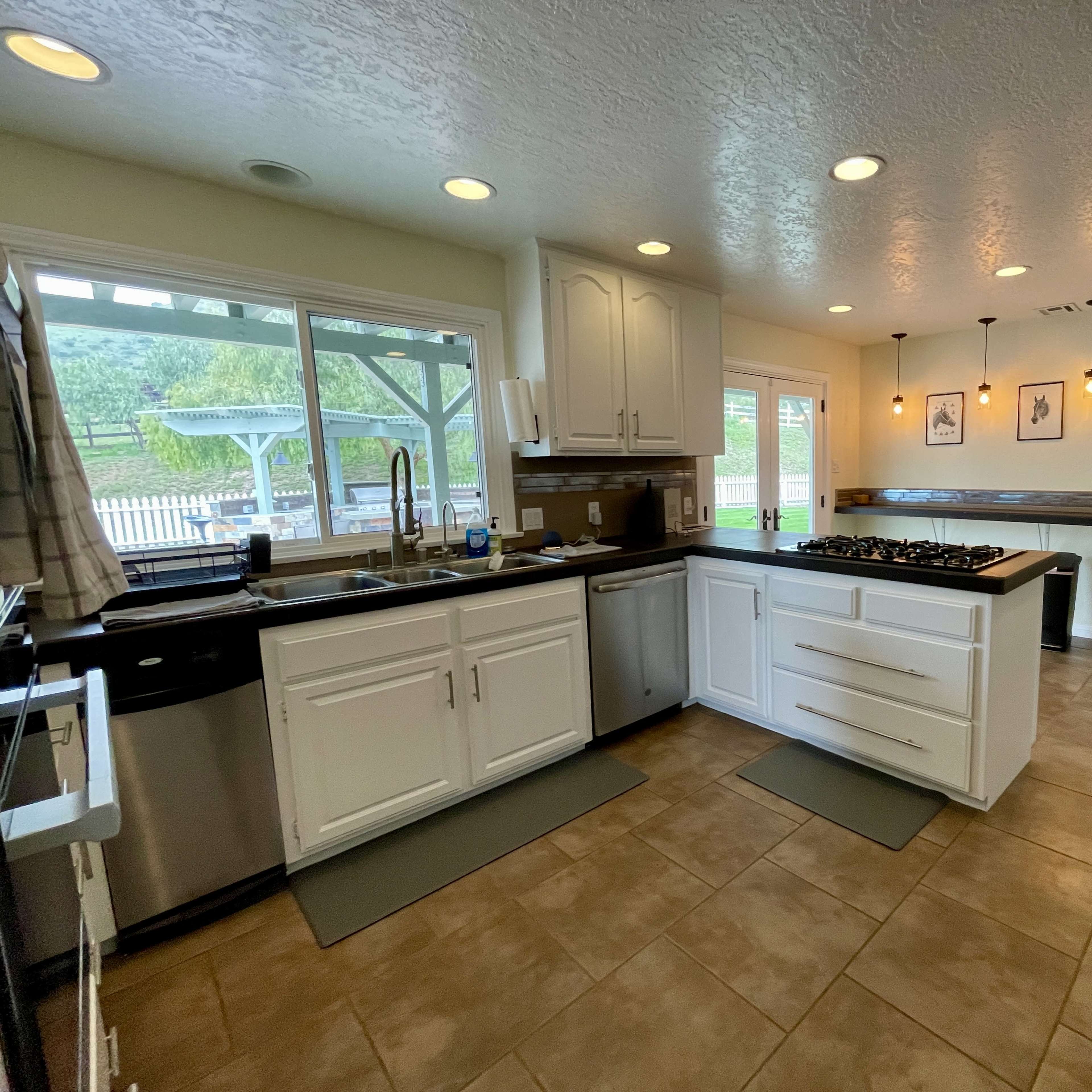 A modern kitchen features white cabinetry, a gas stove, and tile flooring, with a door leading to an outdoor area.