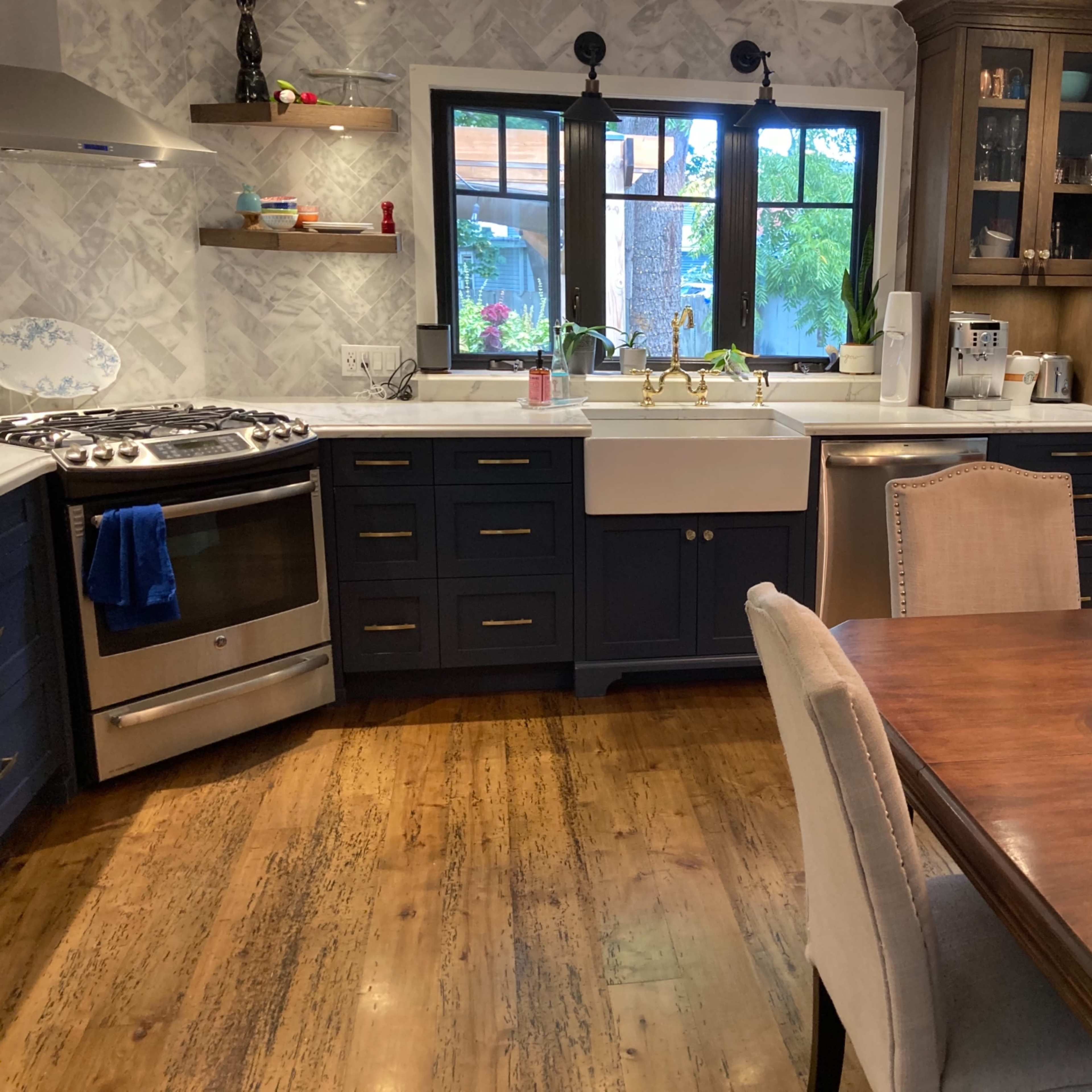 A kitchen with blue cabinets, a farmhouse sink, a stainless steel stove, and a wooden dining table with two aquariums.