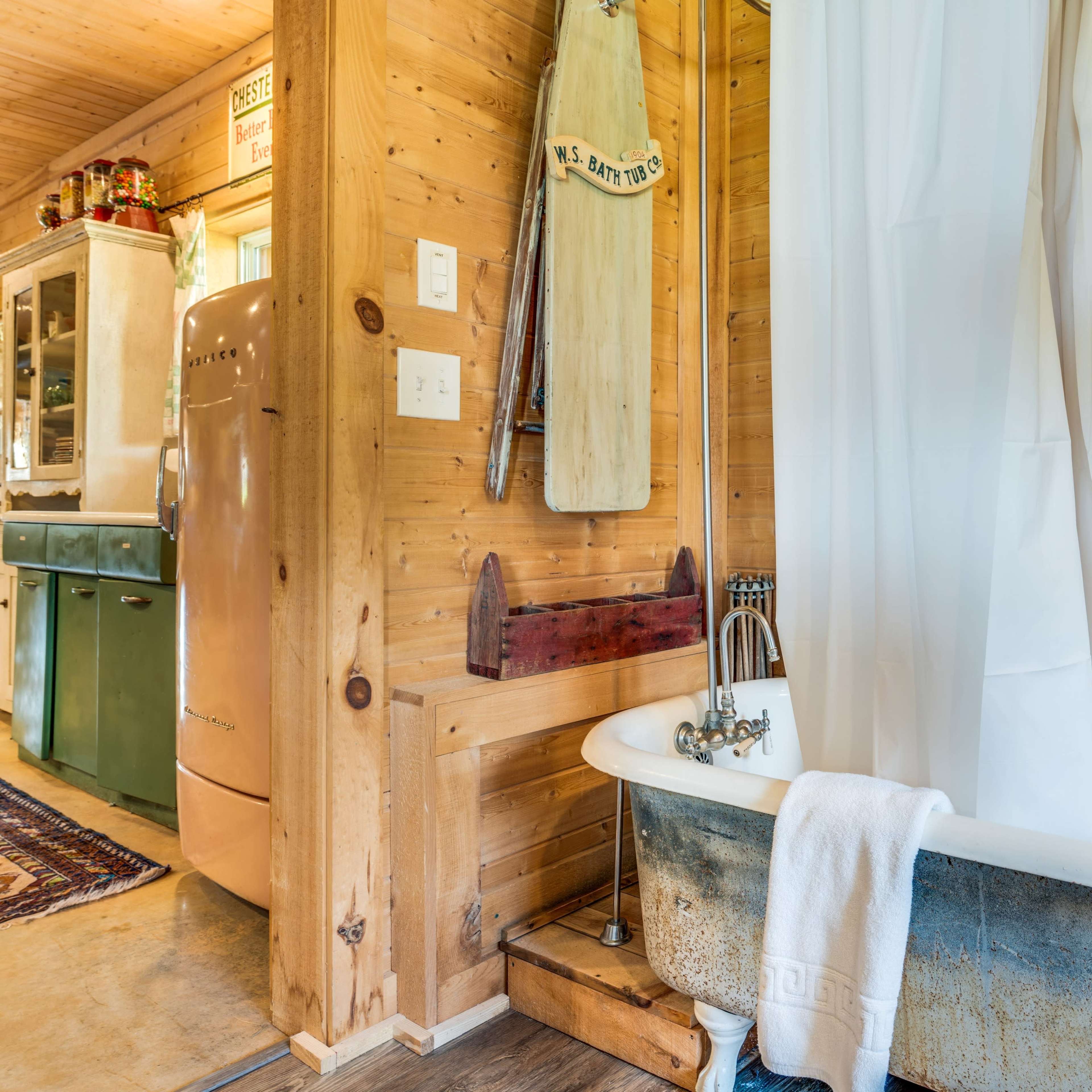 A vintage freestanding bathtub with a white shower curtain is positioned against a wooden wall in a rustic bathroom.