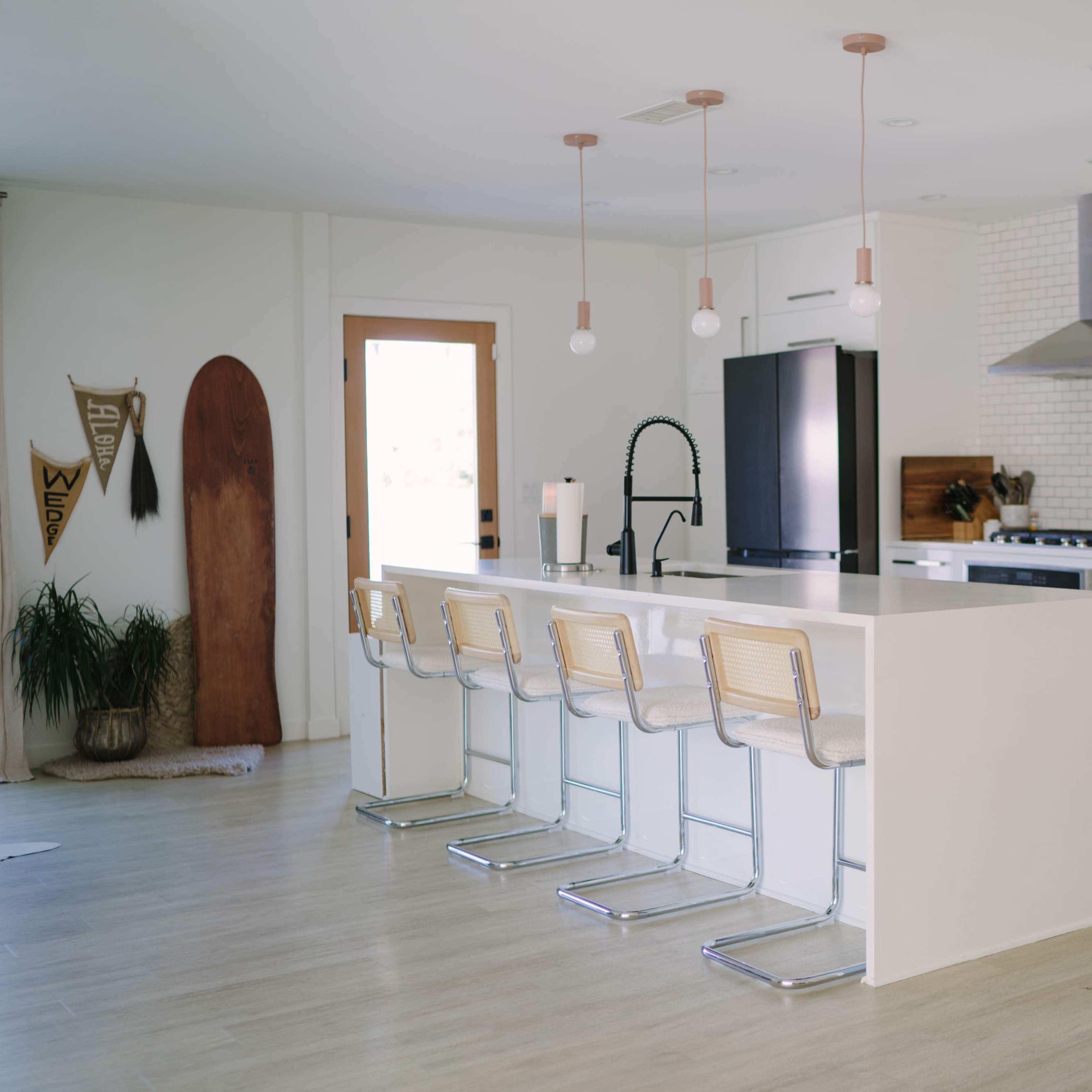 A modern kitchen features a large white island with bar stools, stainless steel appliances, and a wall of white brick.