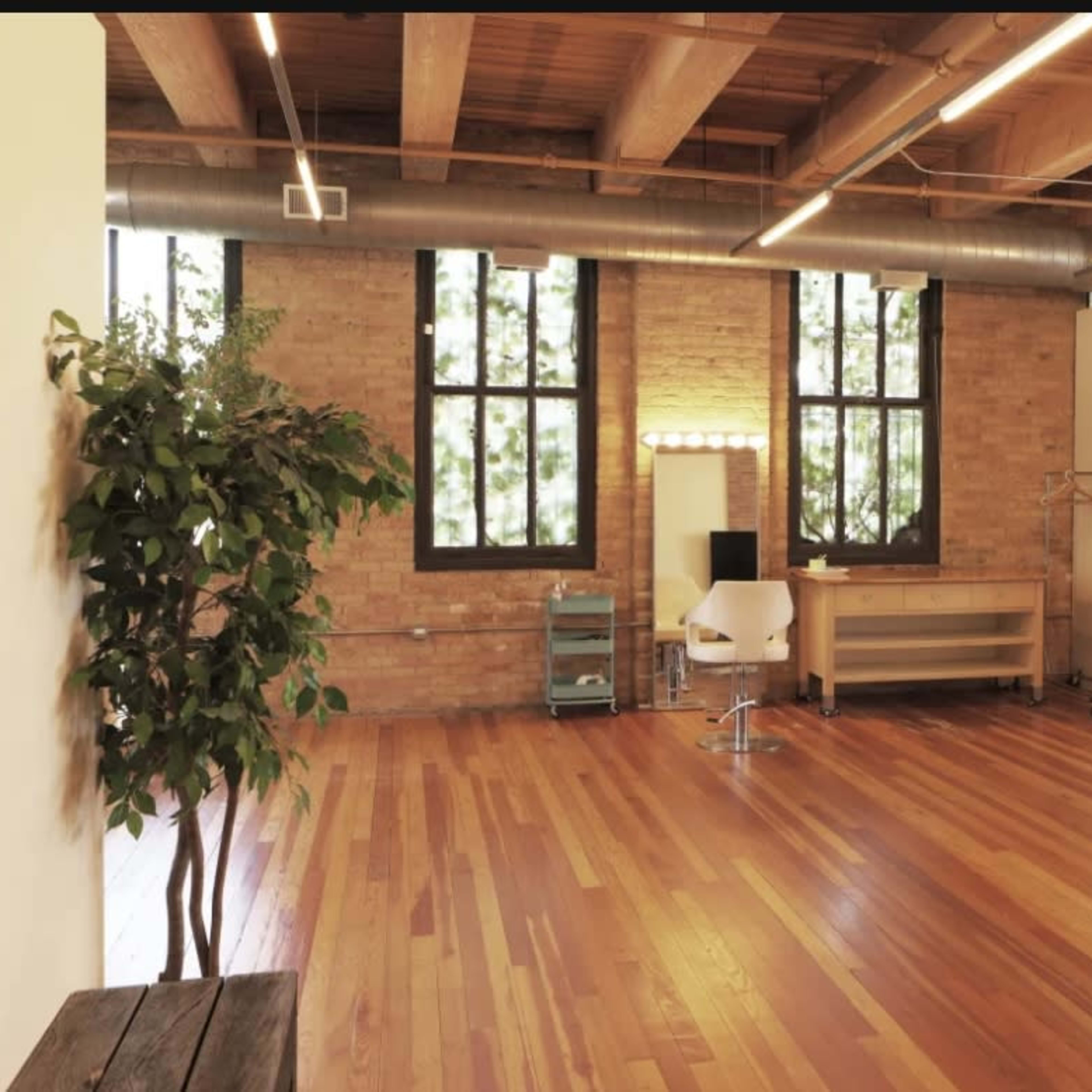 A spacious room with wooden floors, large windows, a makeup station with lights, and a clothing rack.