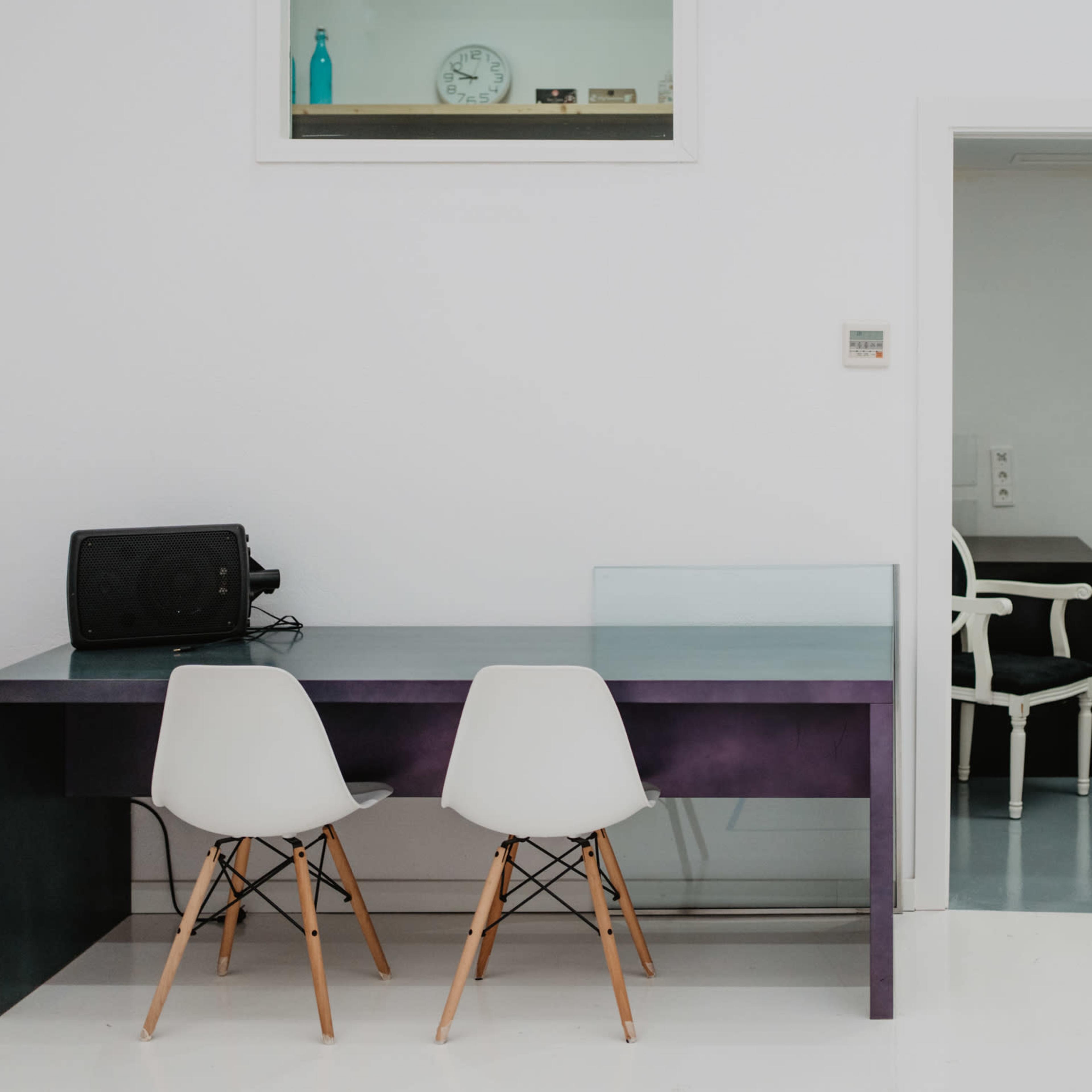 A modern office space features a black table with two white chairs and a door leading to another room in the background.