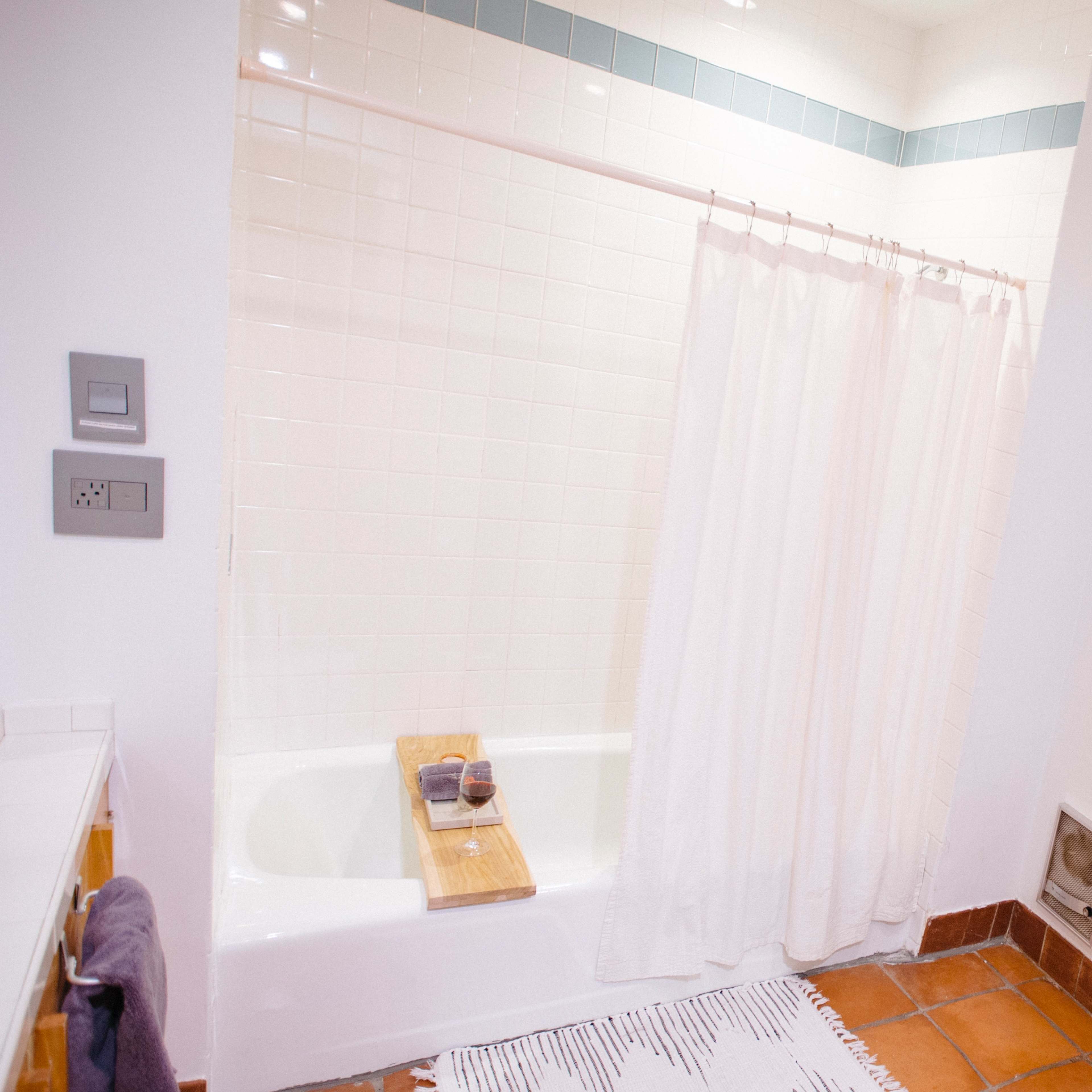 A clean bathroom with a white shower curtain, a bathtub, a wooden bath caddy, and a securely mounted toilet paper holder.