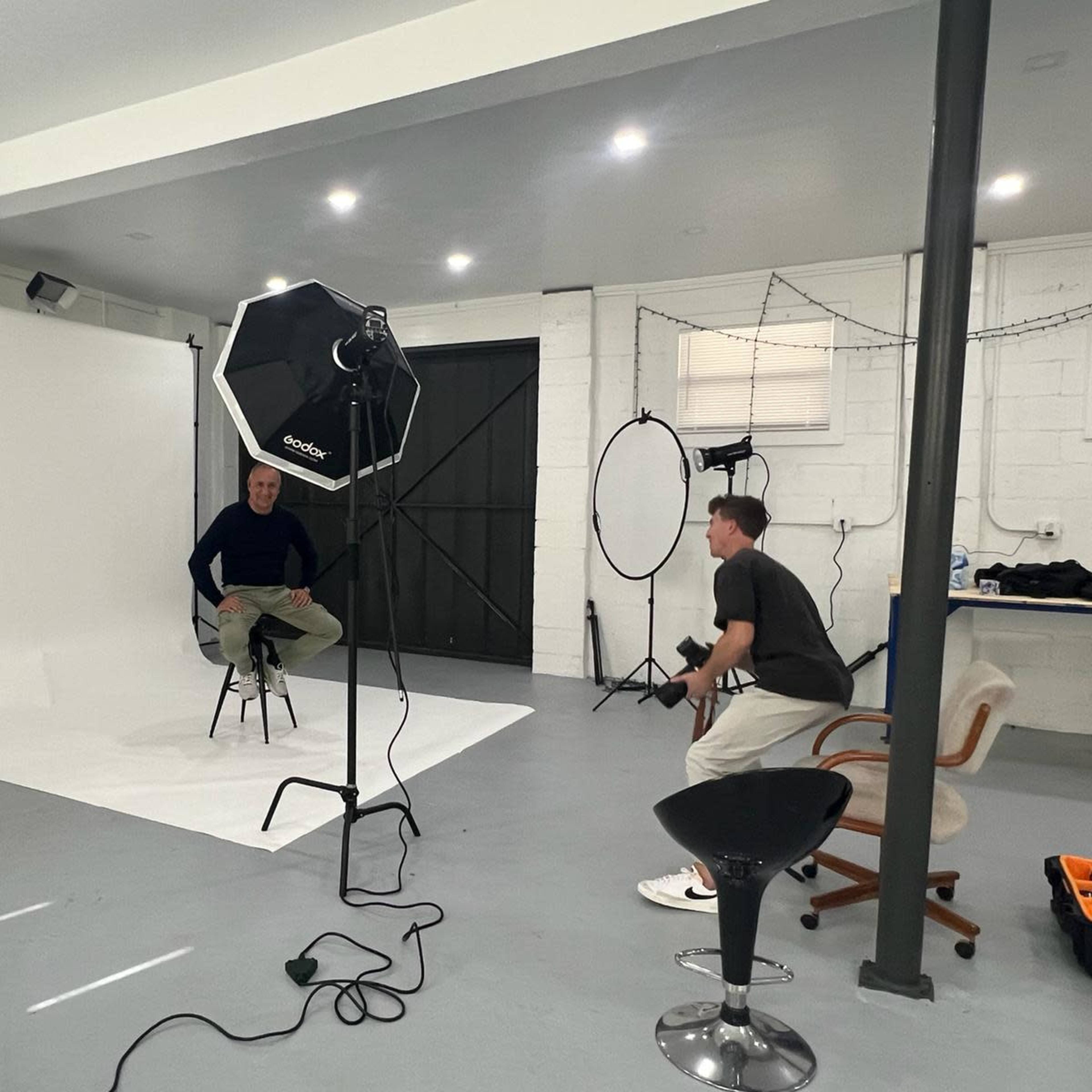 A photography studio features a backdrop, lighting equipment, and two individuals preparing for a photo session.