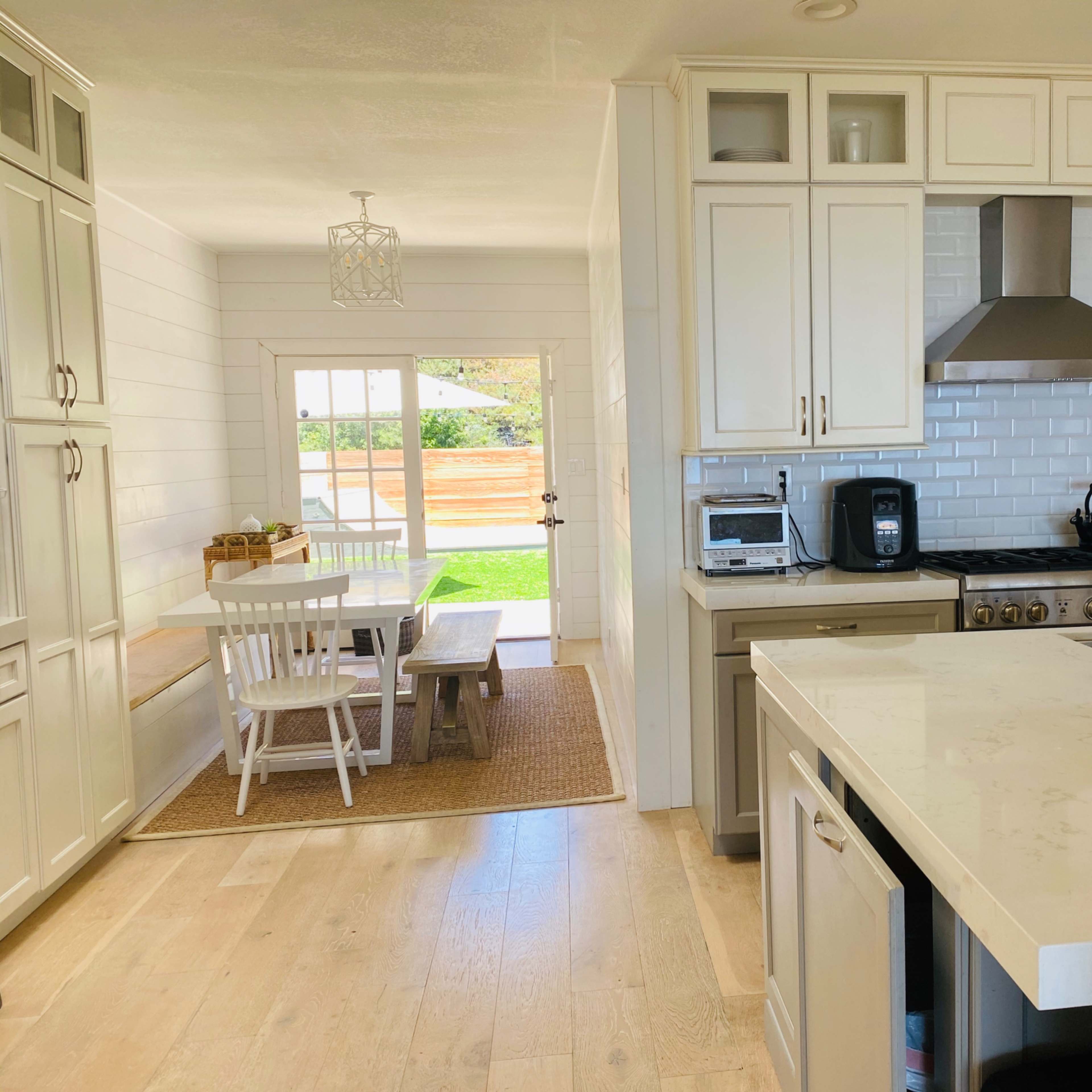 A modern kitchen with white cabinets, a stainless steel stove, and a view of a dining area with a table and chairs through an open doorway.