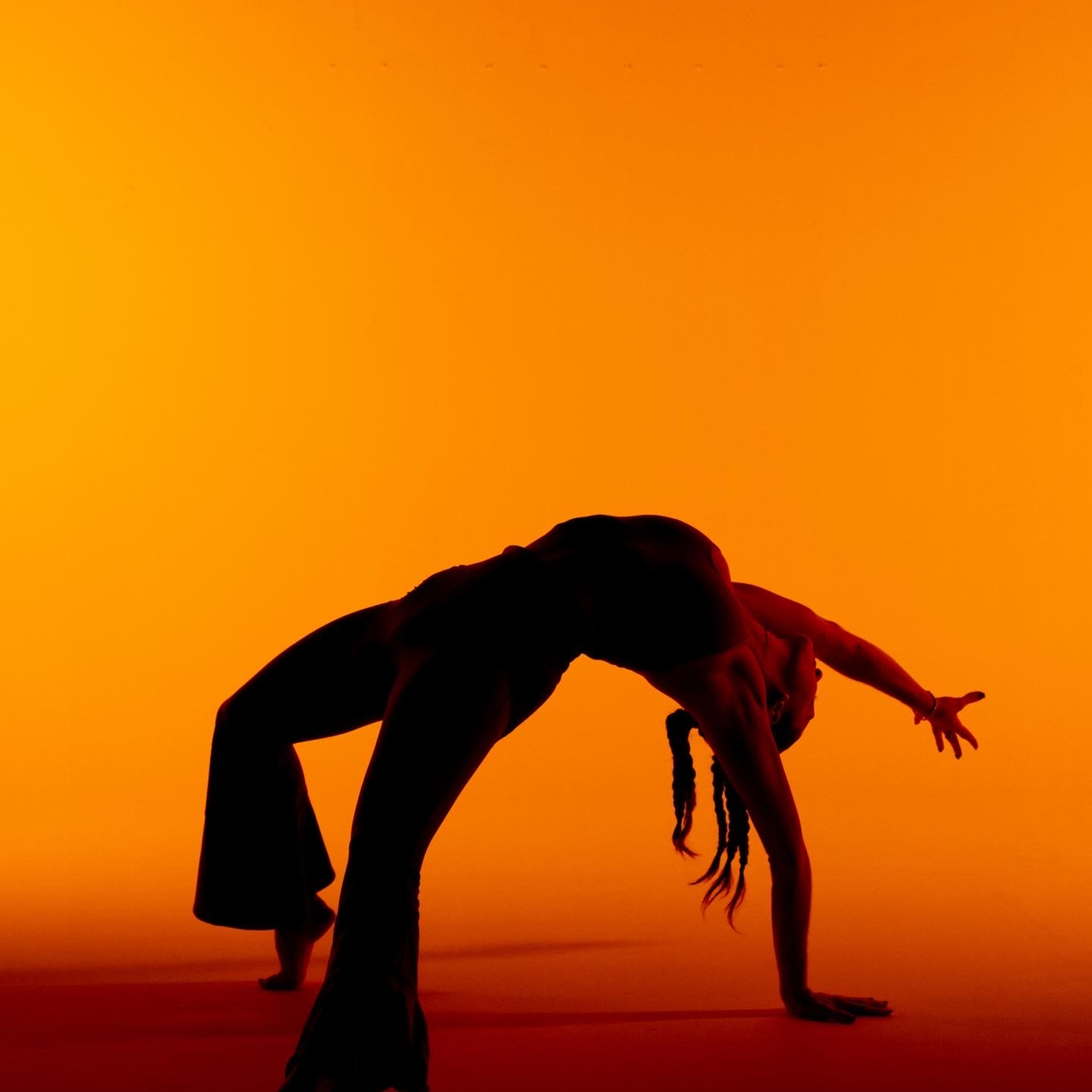 A dancer performs a backbend against an orange backdrop.