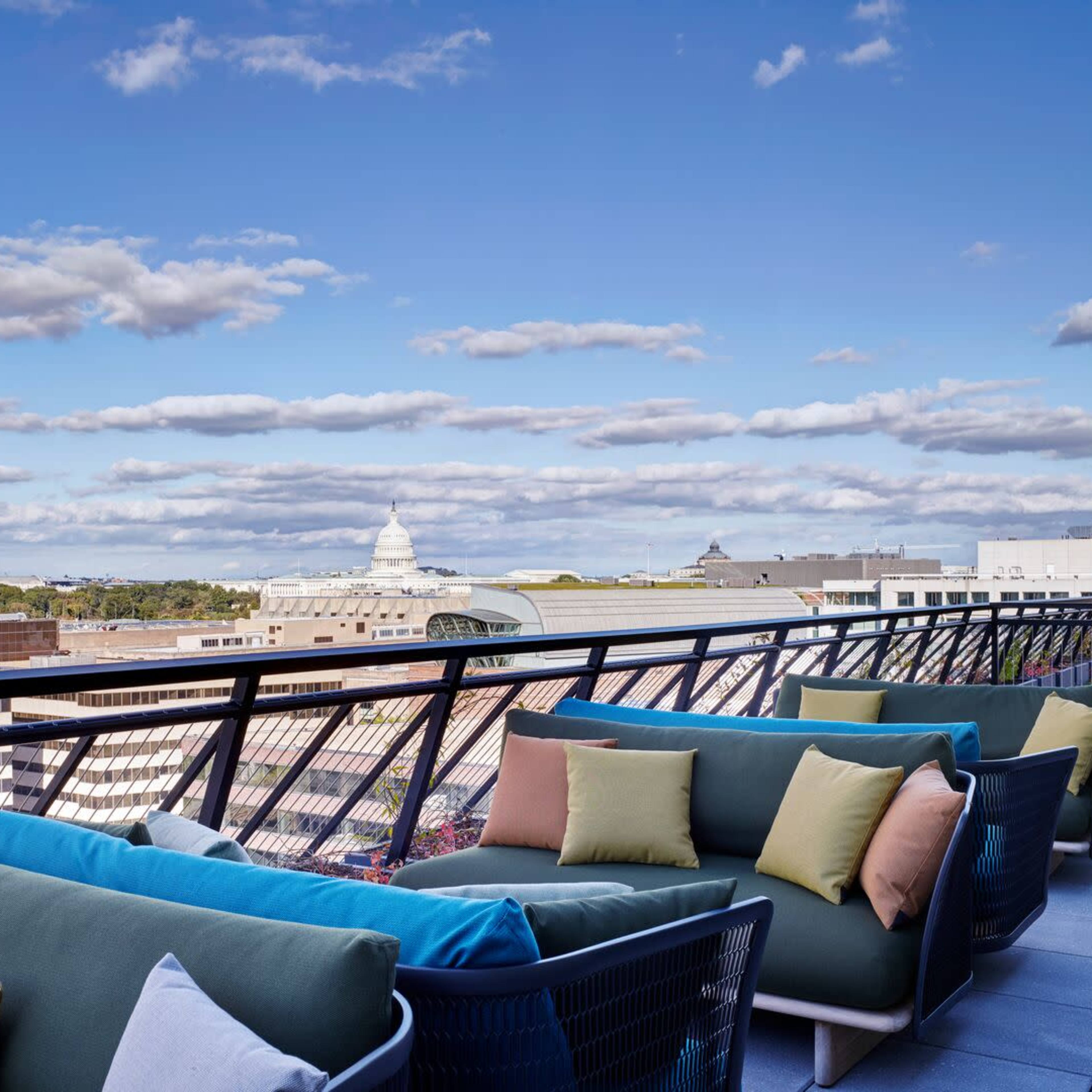 A rooftop terrace with comfortable seating and a view of buildings and a cloudy sky in the background.