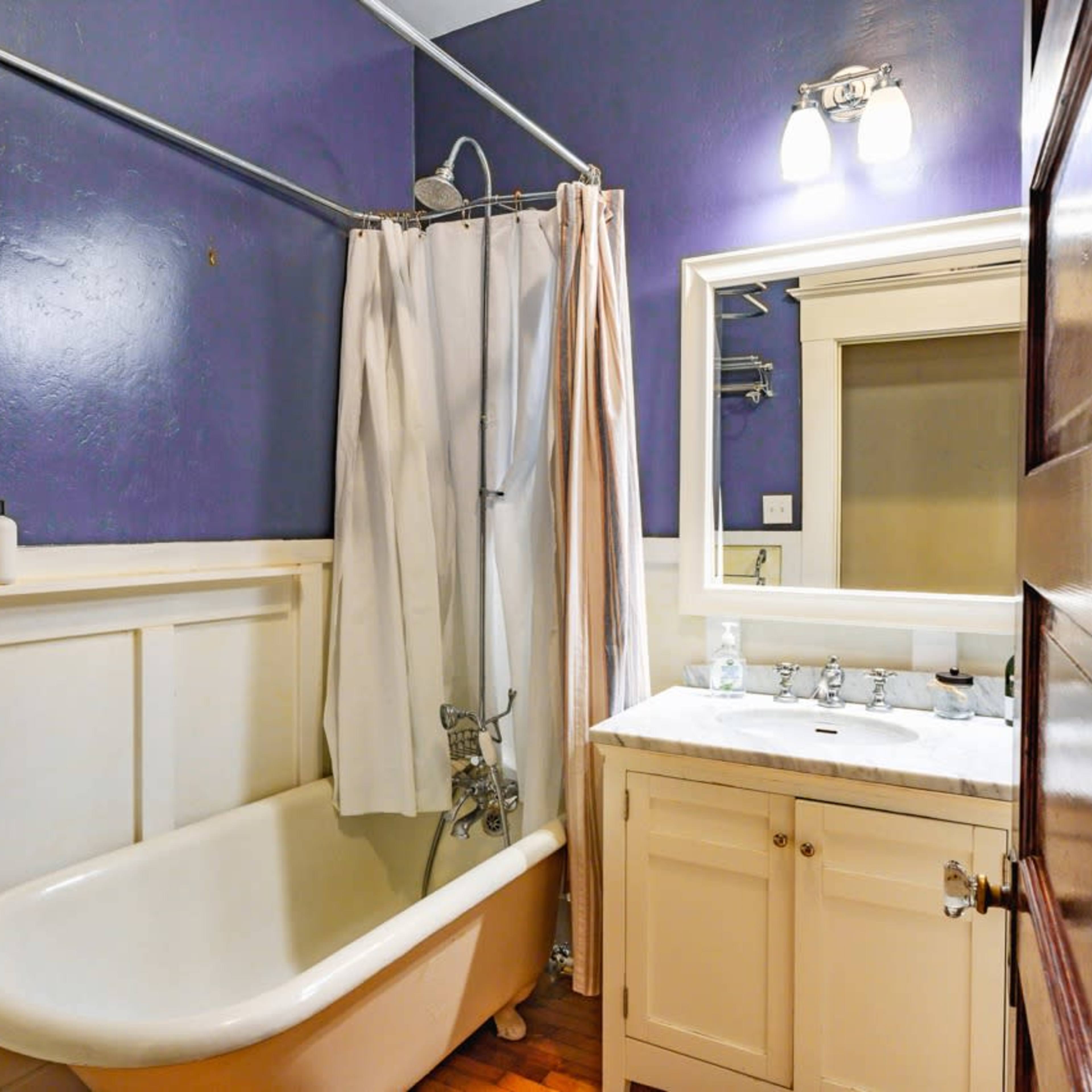 The bathroom features a bathtub with a shower curtain, a wall-mounted mirror above a marble sink, and painted walls in a deep color.