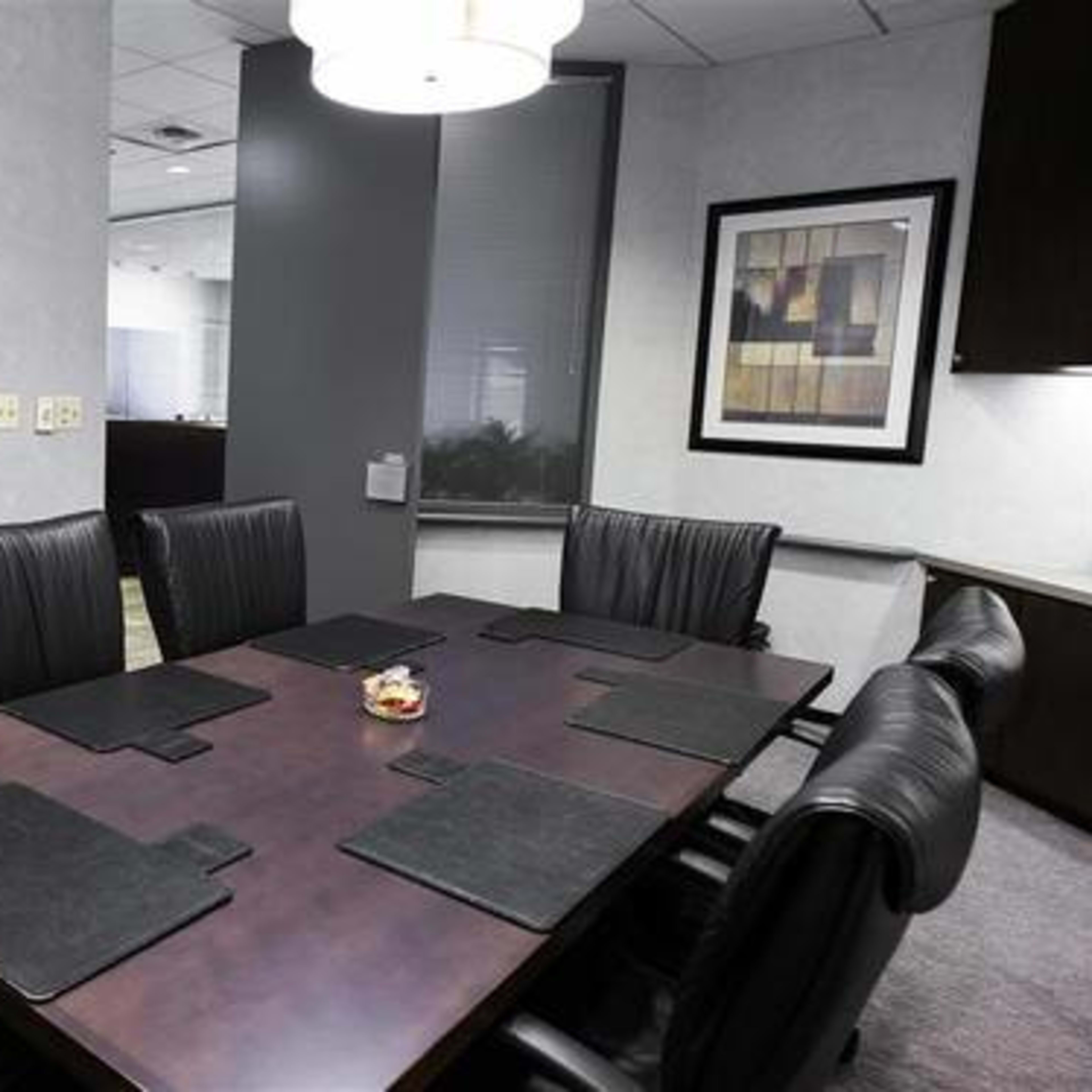 A conference room with a large table surrounded by leather chairs, a television mounted on the wall, and a decorative piece framed on the adjacent wall.
