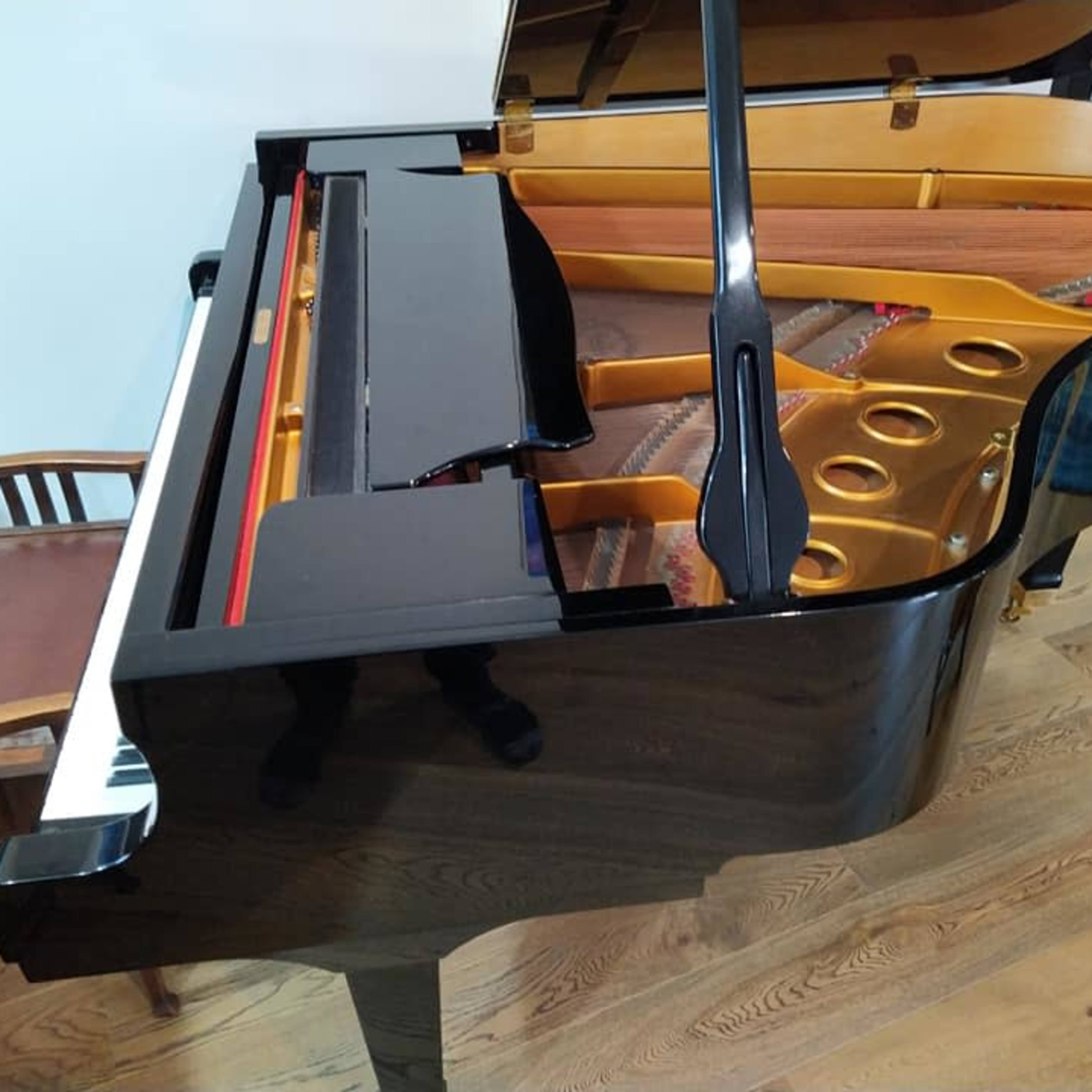 A black grand piano is positioned next to a wooden chair in a room with hardwood floors.