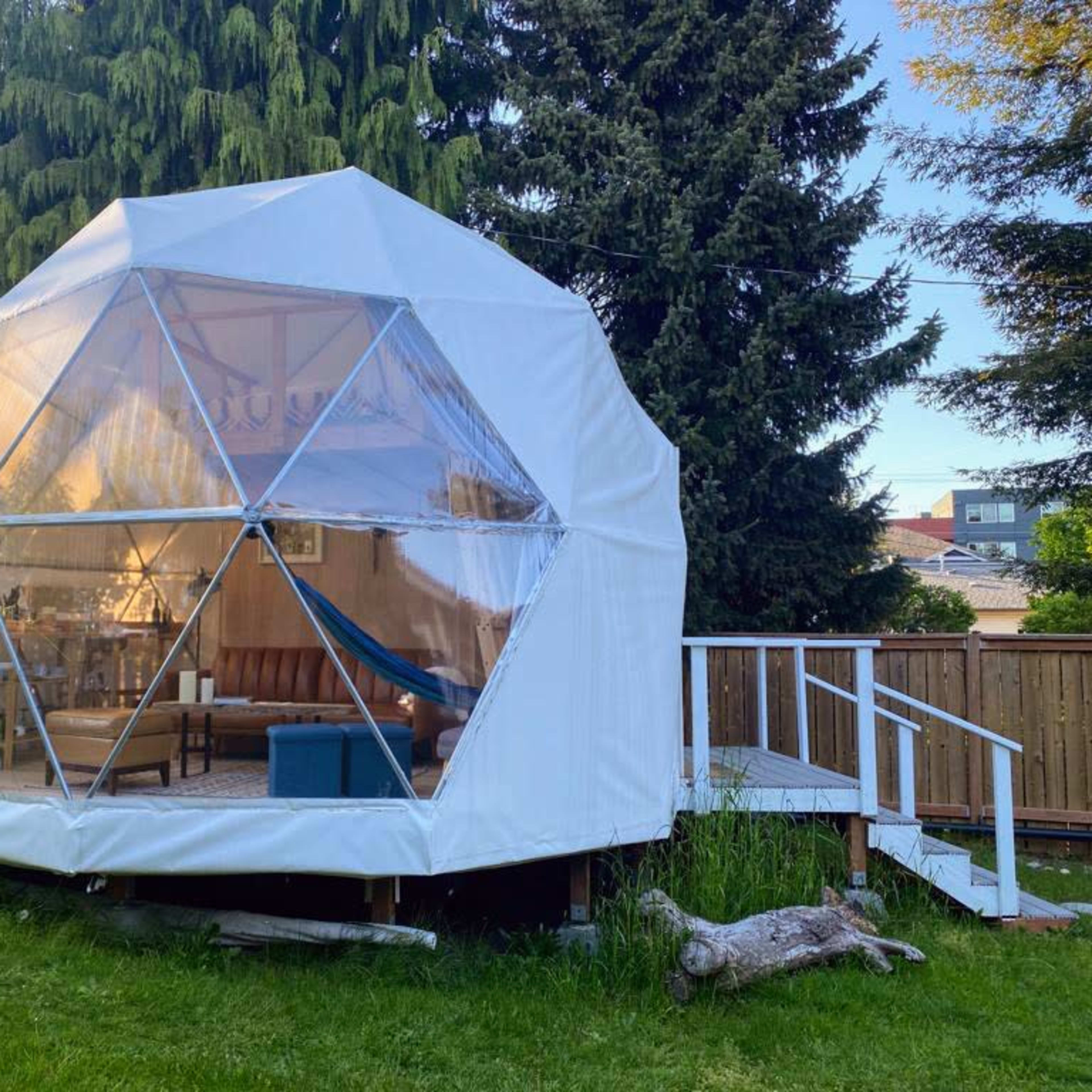 A geodesic dome structure in a backyard, featuring clear panels and a wooden deck with steps.
