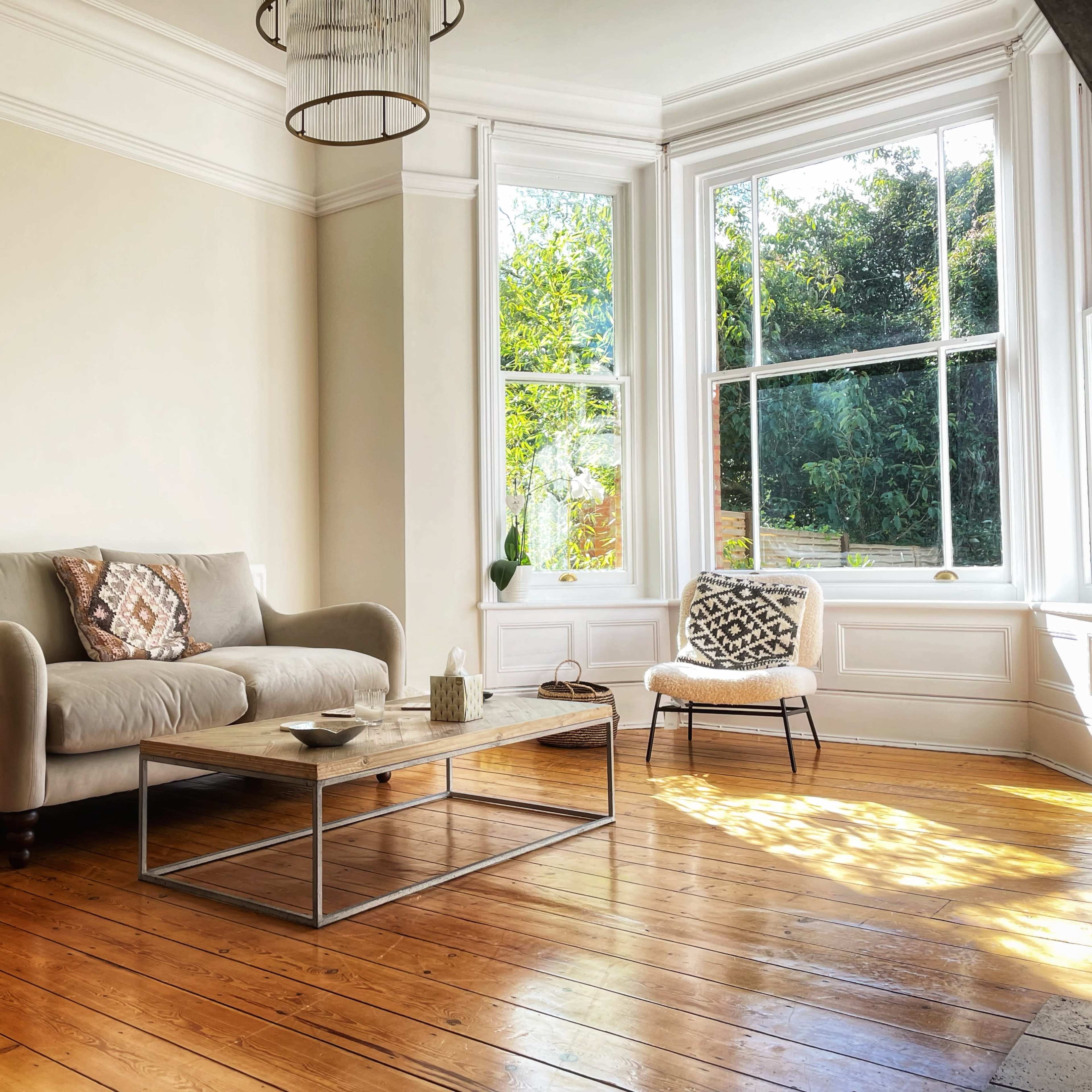 A minimalist living room with a beige sofa, a wooden coffee table, and large windows that allow natural light to flood the space.