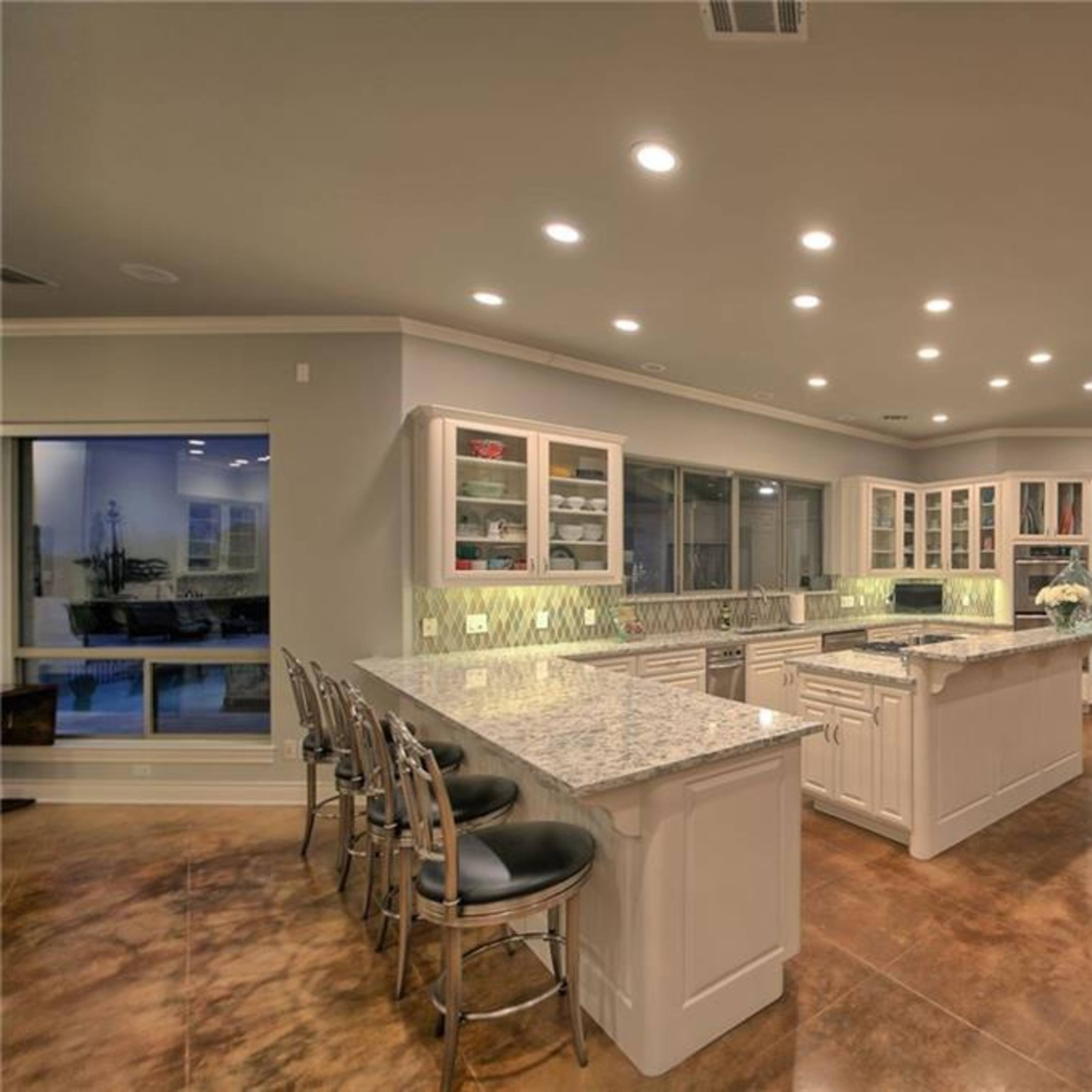 The kitchen features a large island with granite countertops, white cabinetry, and stainless steel appliances, illuminated by recessed lighting.