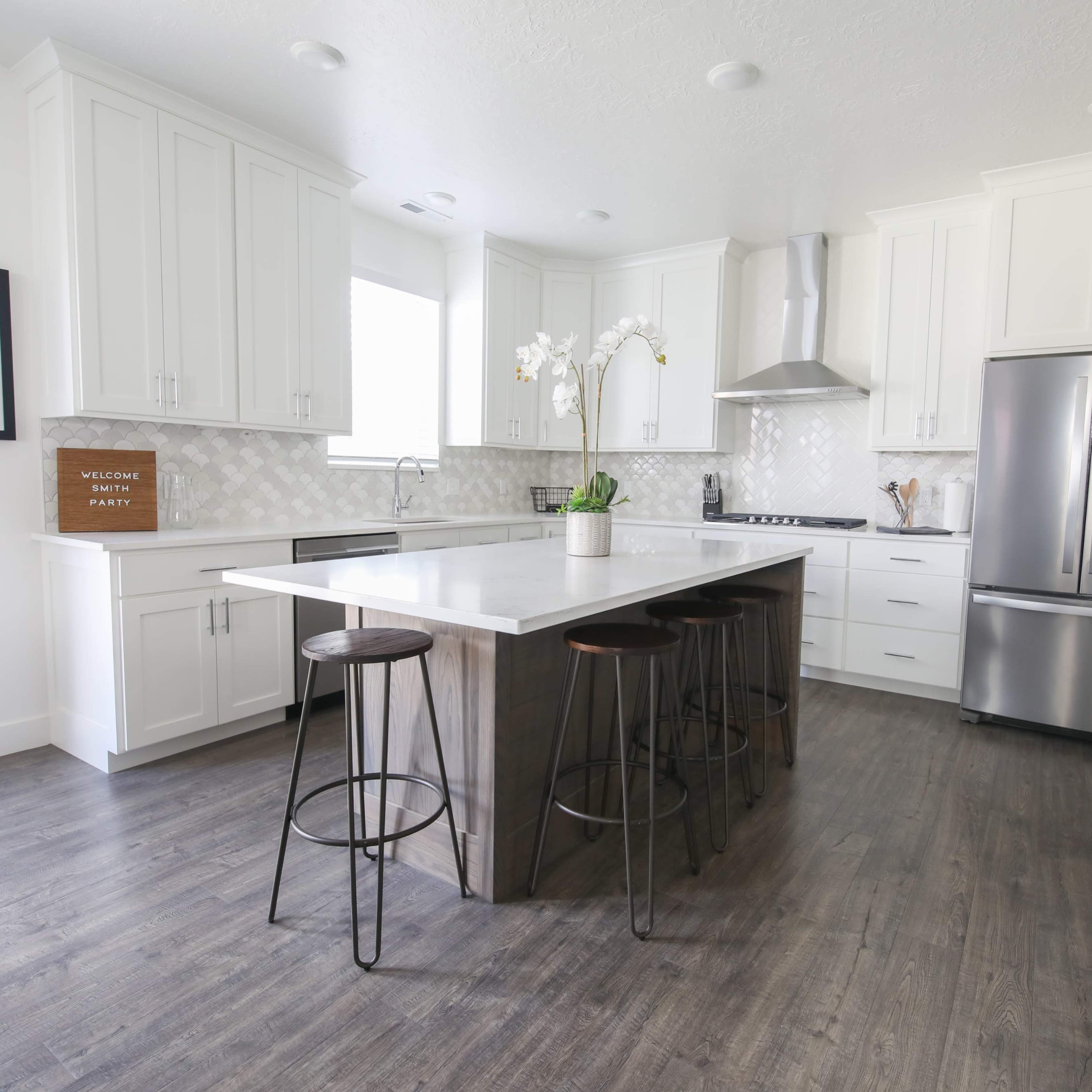 A modern kitchen featuring white cabinets, a gray island with bar stools, and stainless steel appliances.