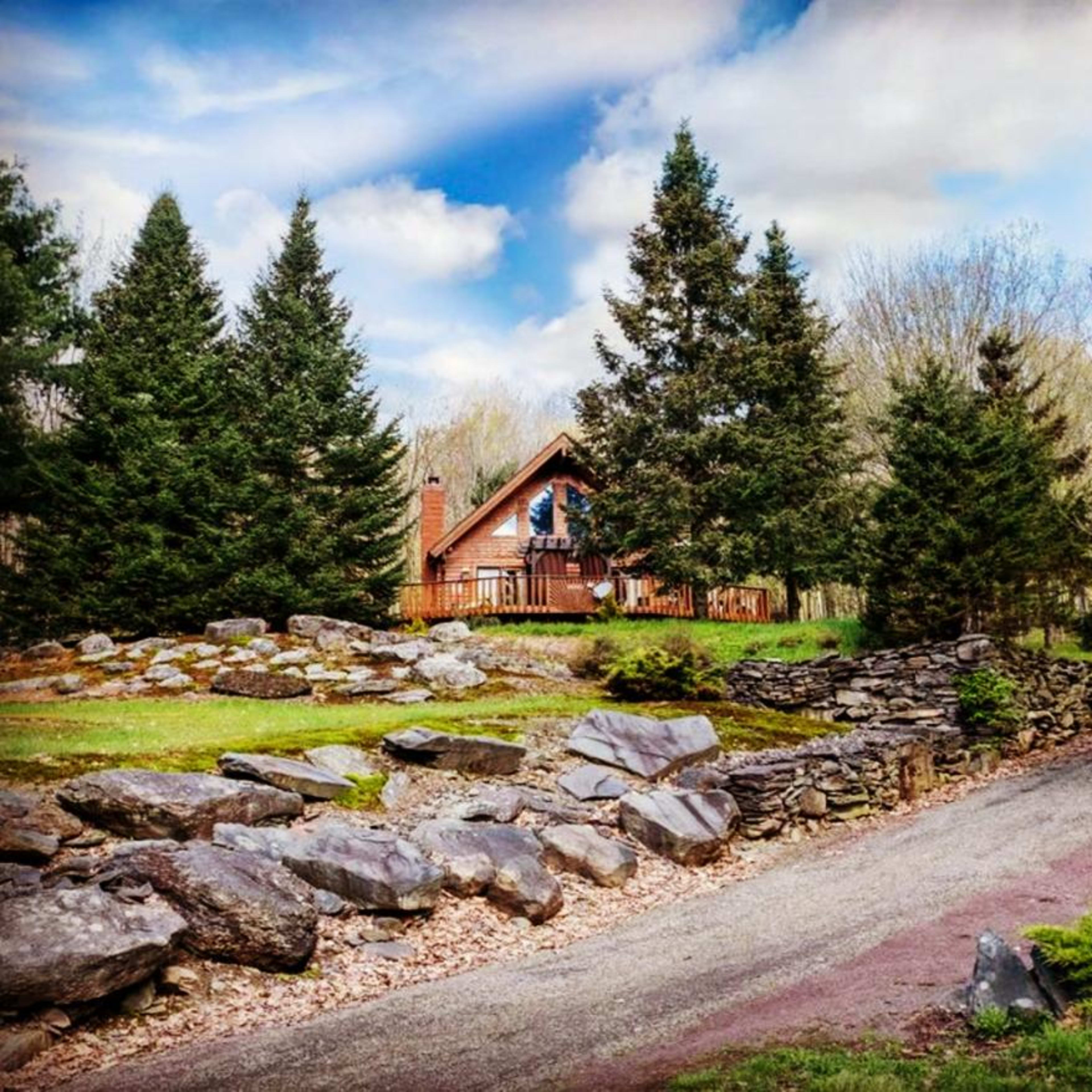 A gravel path leads to a wooden cabin among large rocks and tall evergreen trees.