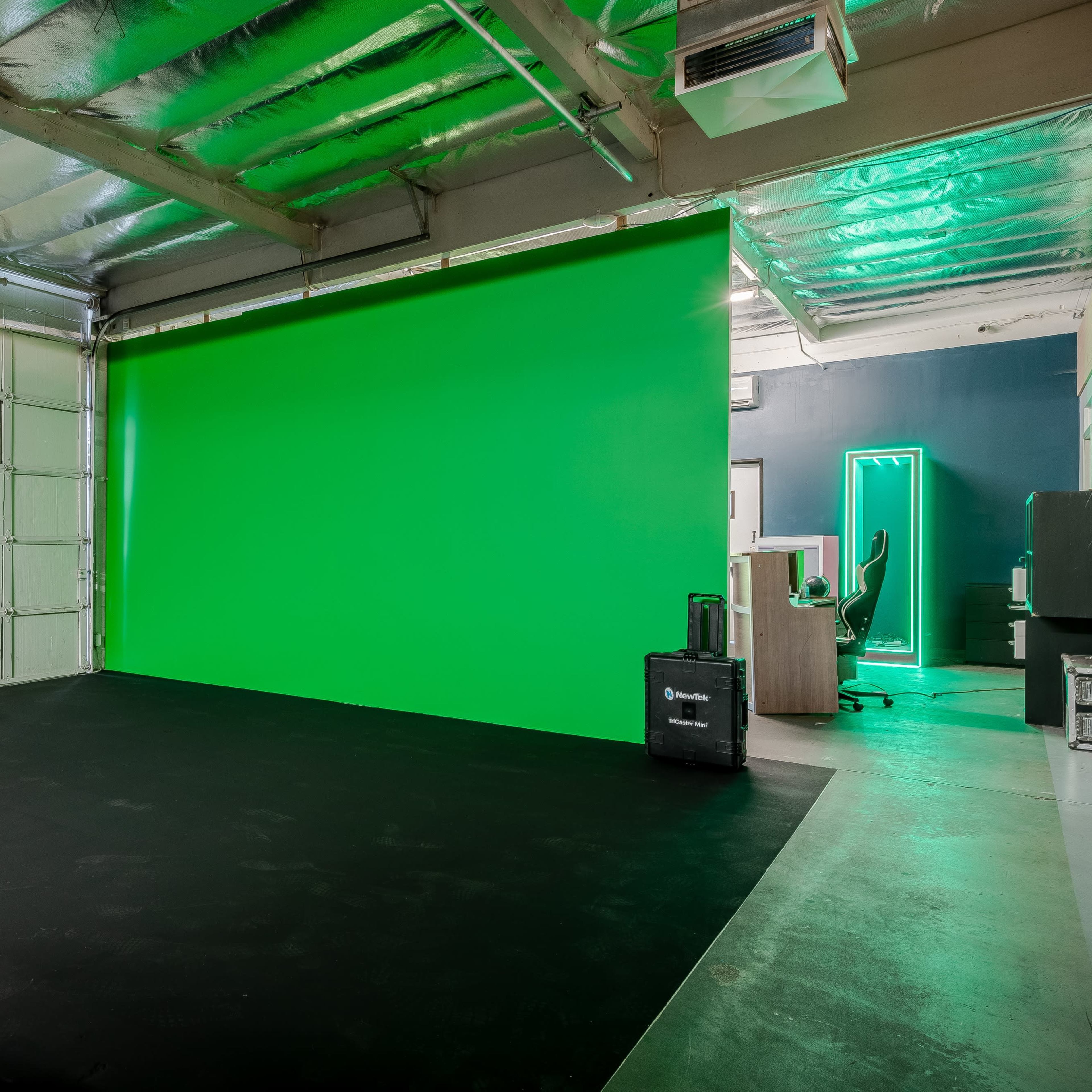 A room with a green screen wall, a black floor, and a garage door on one side.