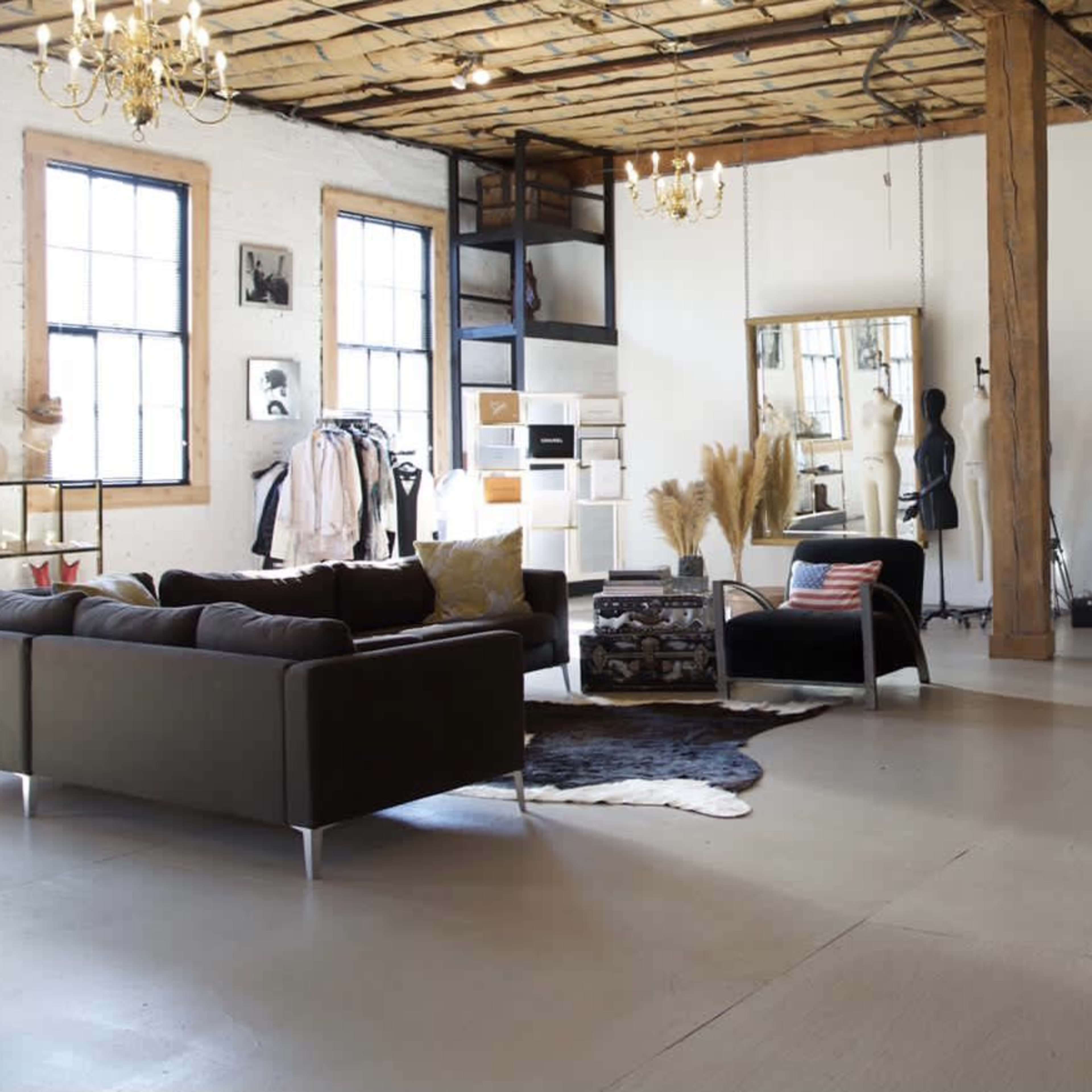 A spacious loft-style interior featuring a living area with a dark sofa, a dining area with a bar counter, and large windows that allow natural light to enter.