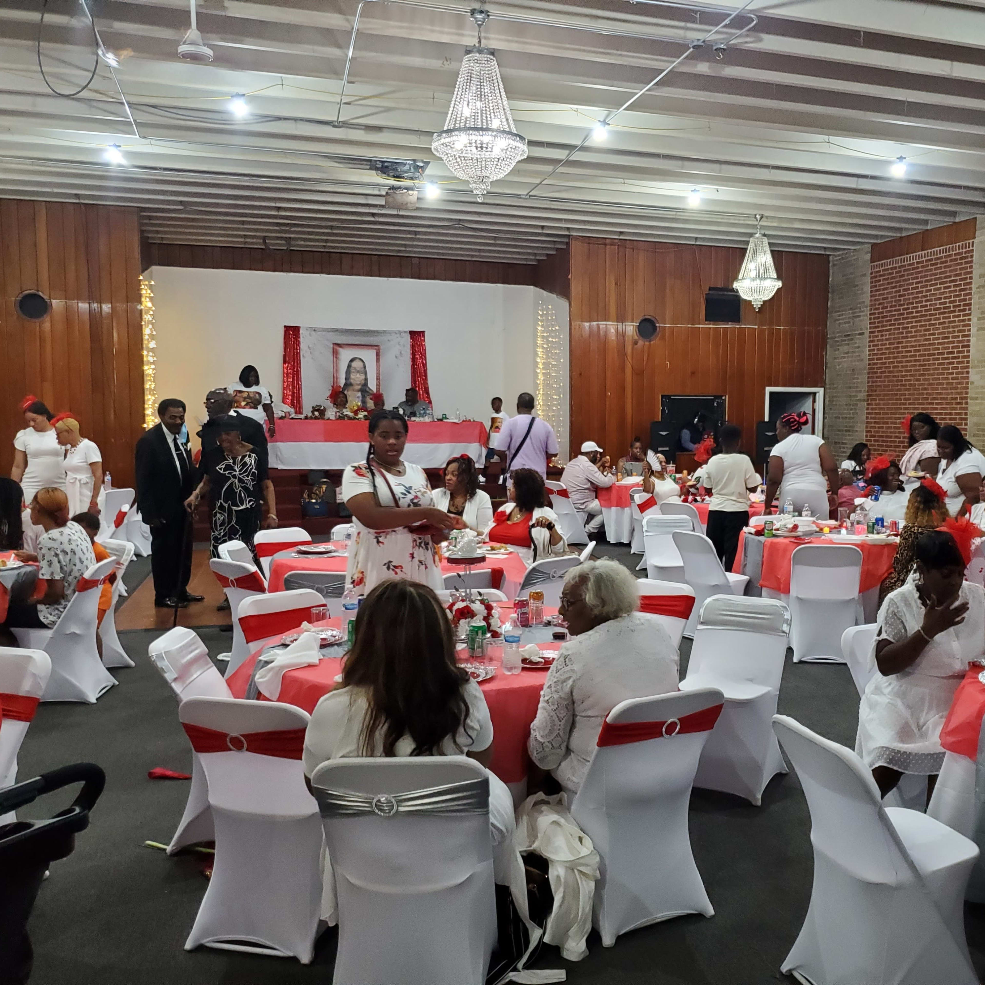 A large banquet hall is decorated with red and white tablecloths, where guests are seated at tables and mingling during an event.