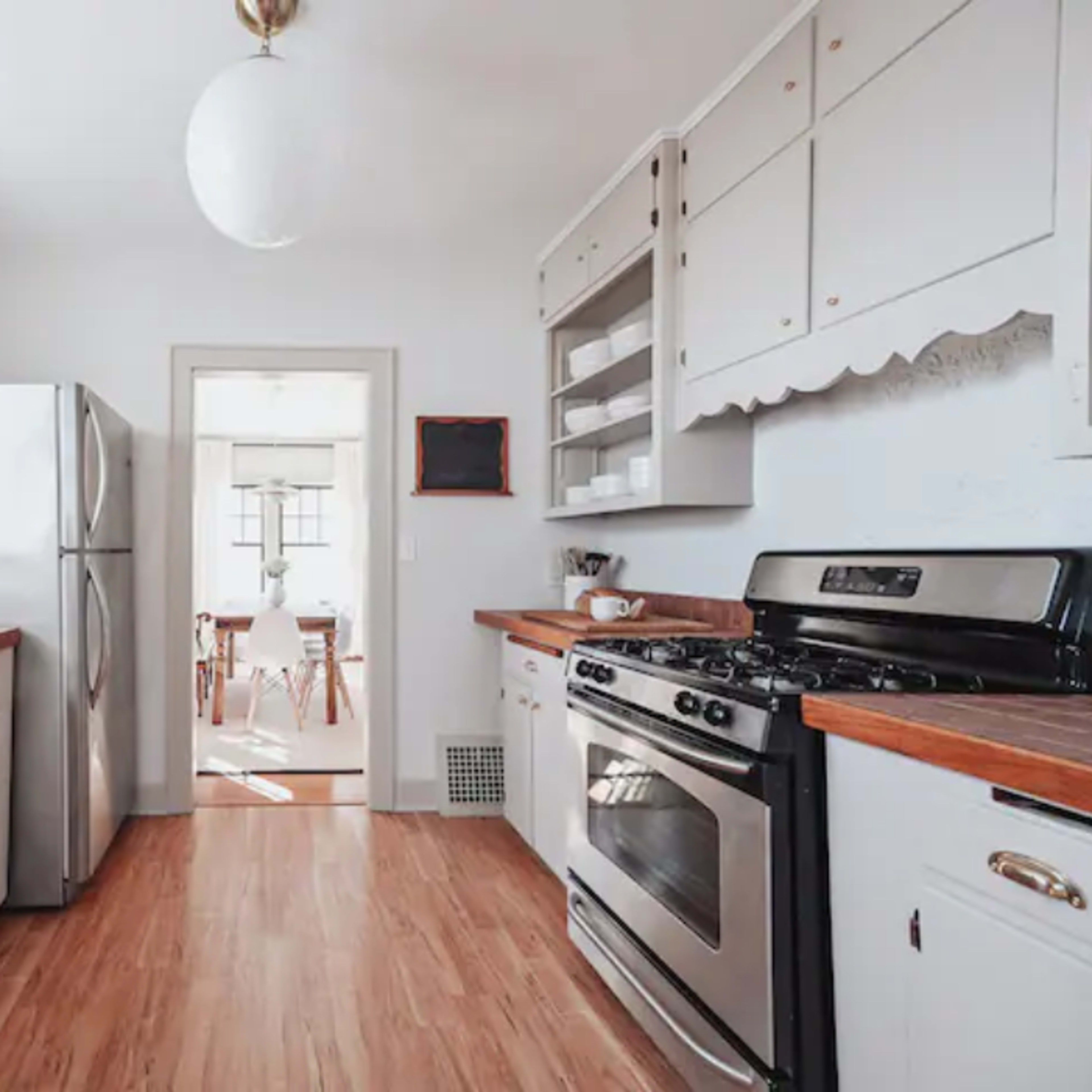 A tidy kitchen featuring stainless steel appliances, wooden countertops, and white cabinetry, with a doorway leading to a dining area.