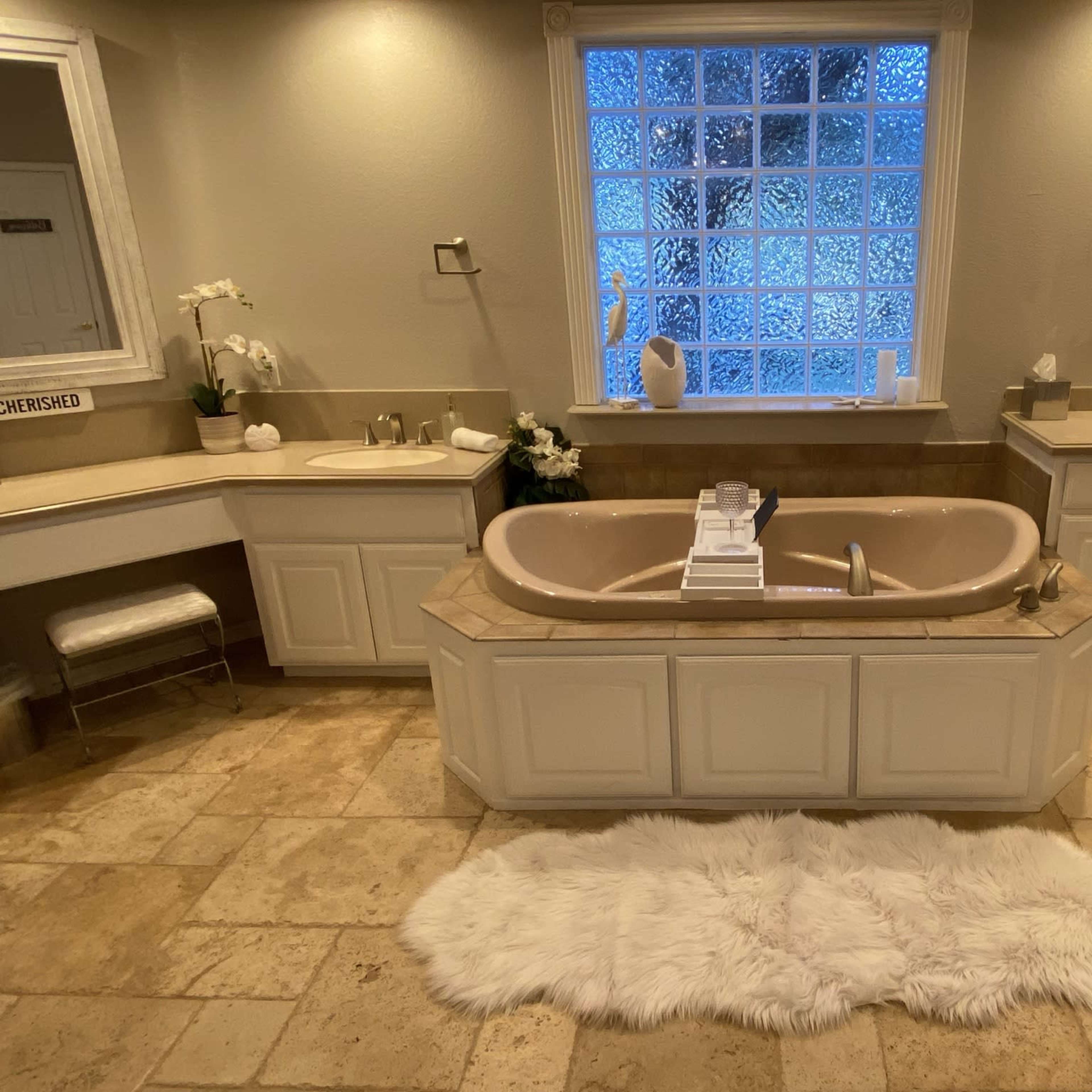 A spacious bathroom featuring a large, tan bathtub in the center, surrounded by light-colored cabinetry and a tiled floor.