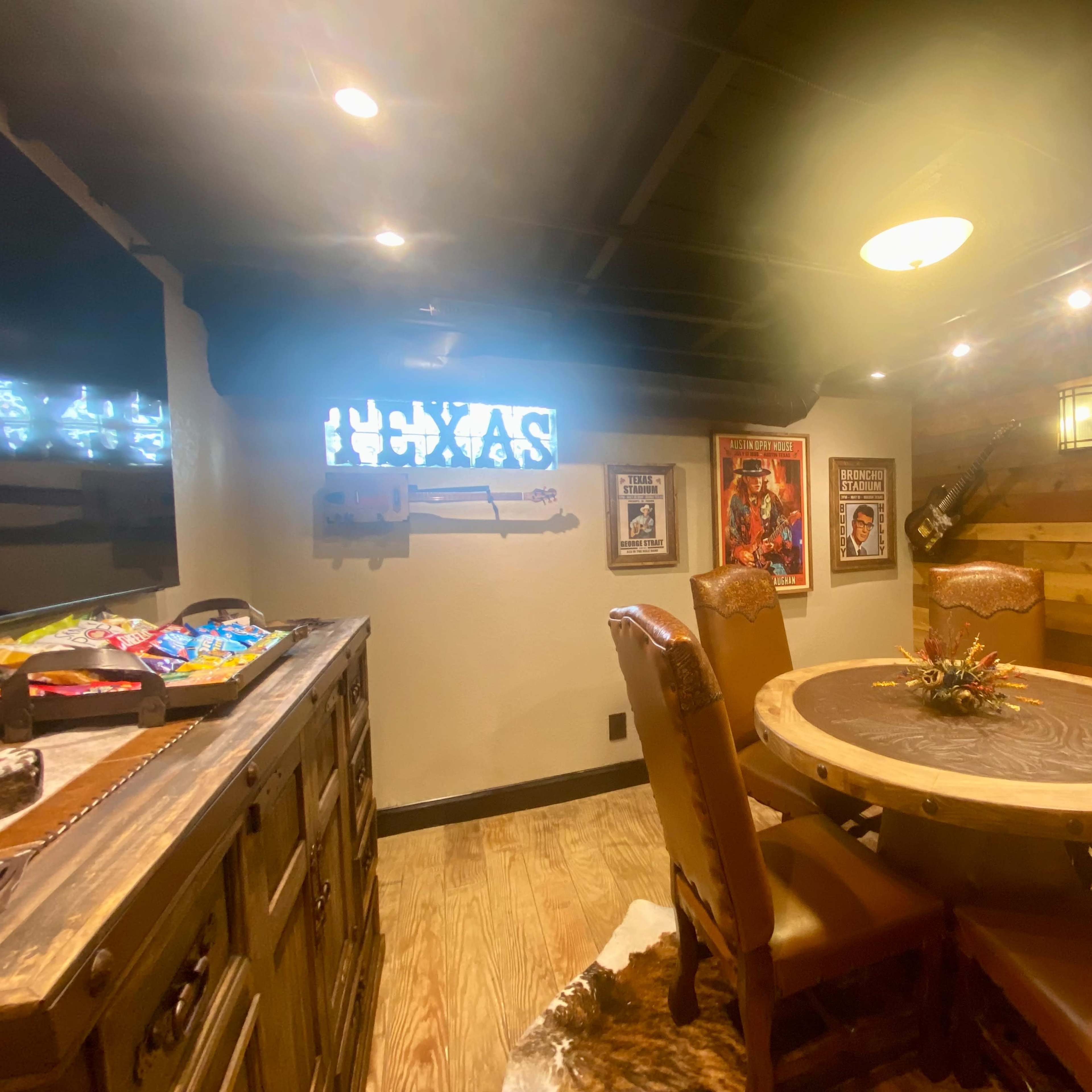 A rustic dining area with a circular wooden table surrounded by leather chairs, adorned with framed posters and decorative items on the walls.