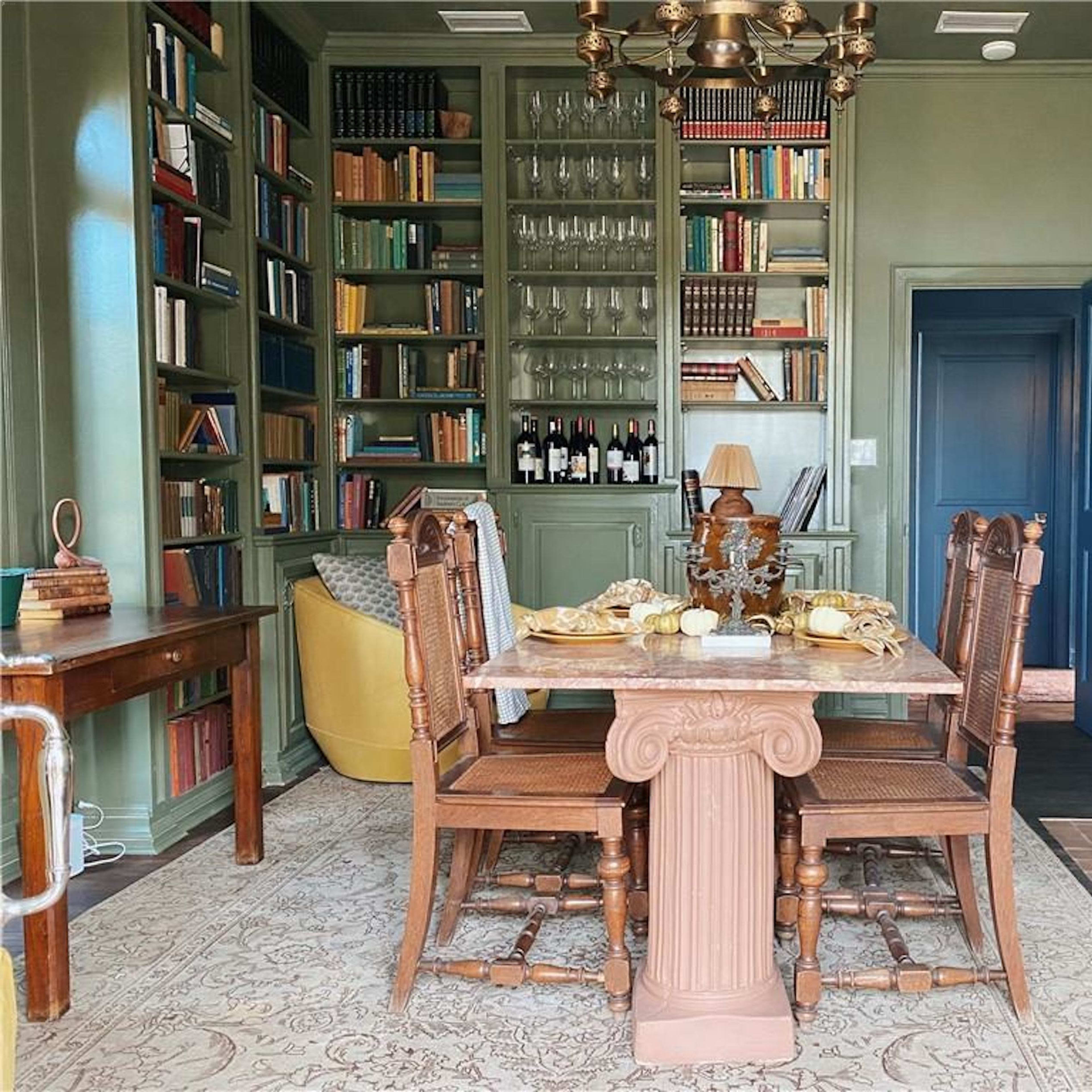 A dining area with a rectangular table surrounded by wooden chairs, bookshelves filled with books along the walls, and a small fireplace.