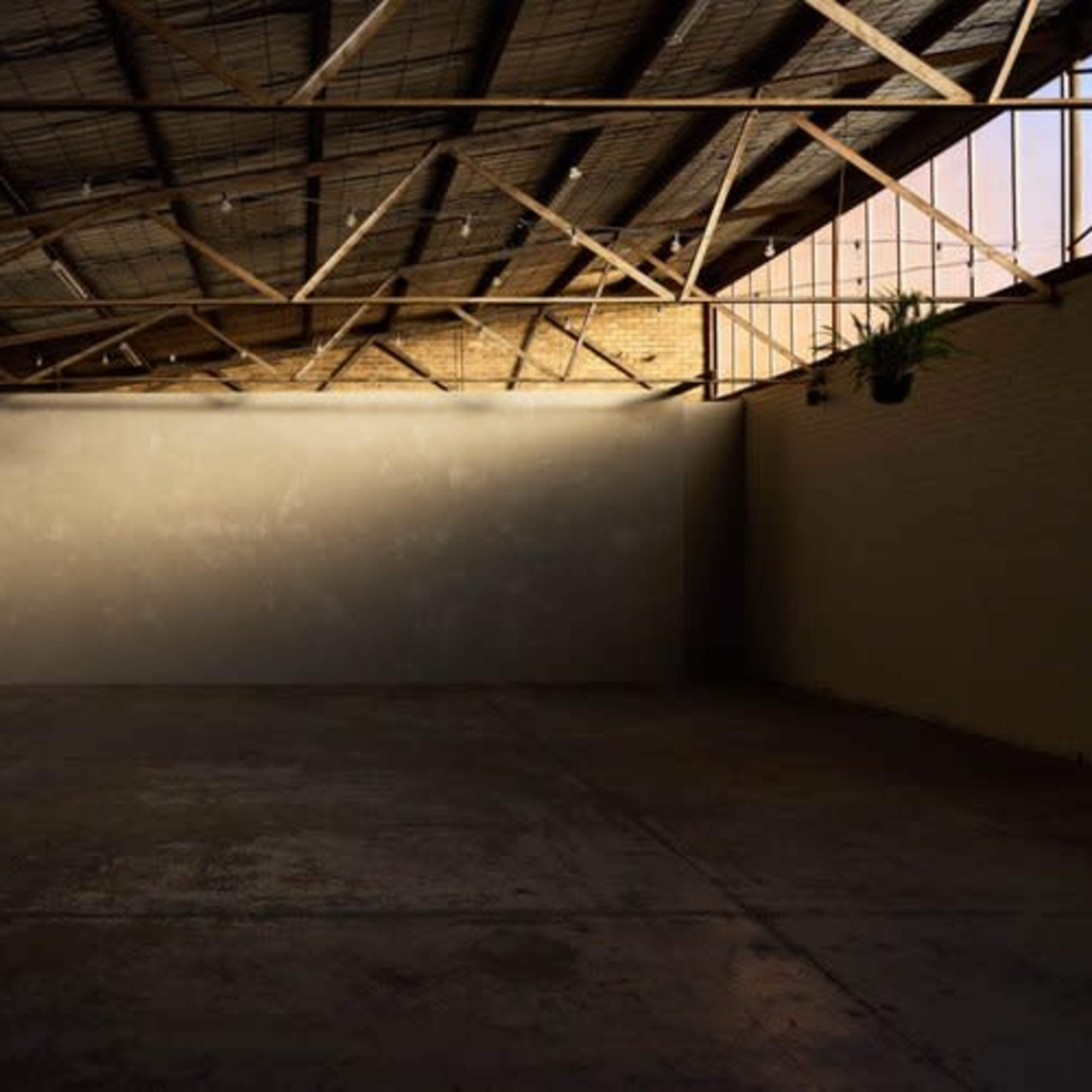 A spacious, empty room with a concrete floor and exposed wooden beams overhead.