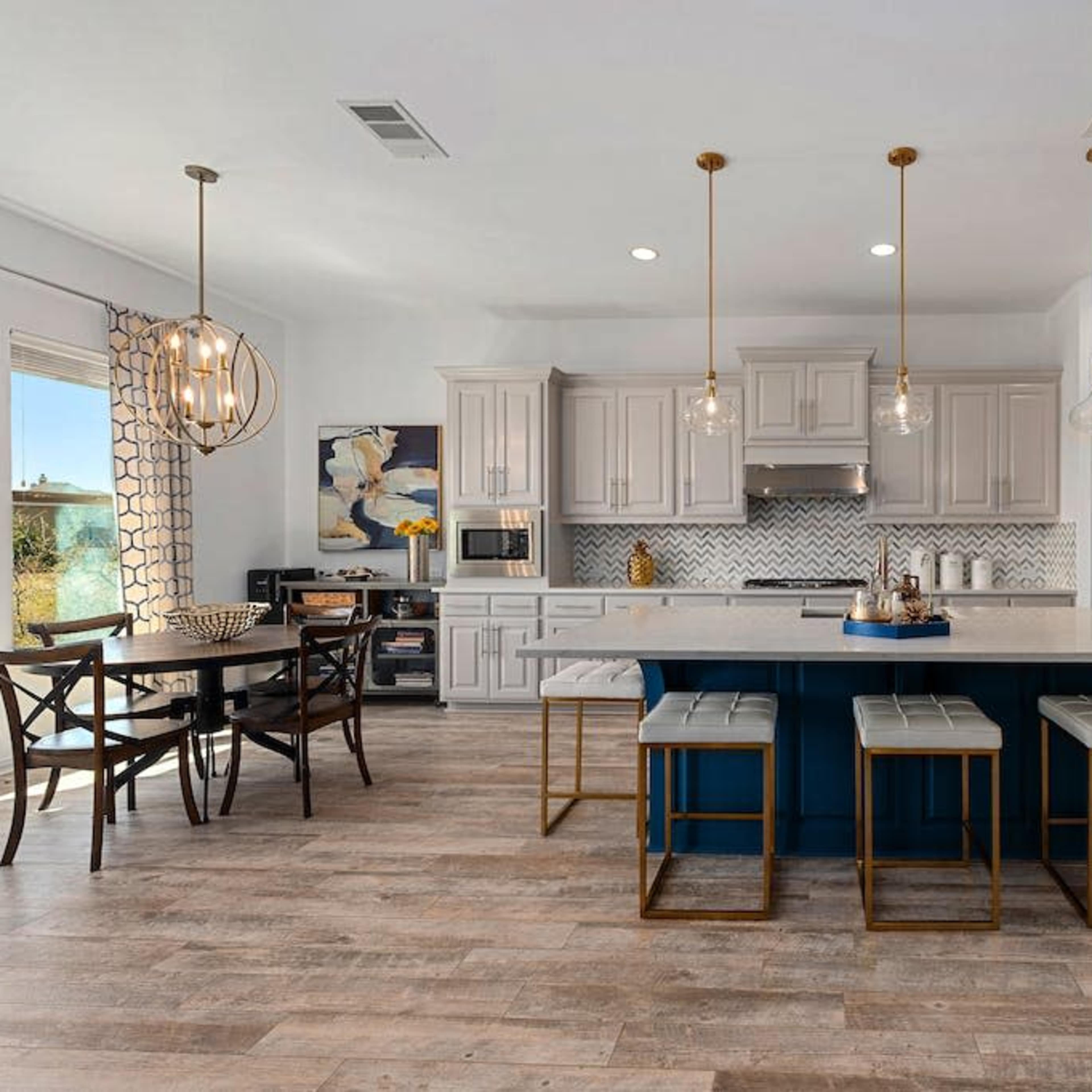 A modern kitchen with light cabinetry, a large island with seating, and a dining area featuring a contemporary light fixture.