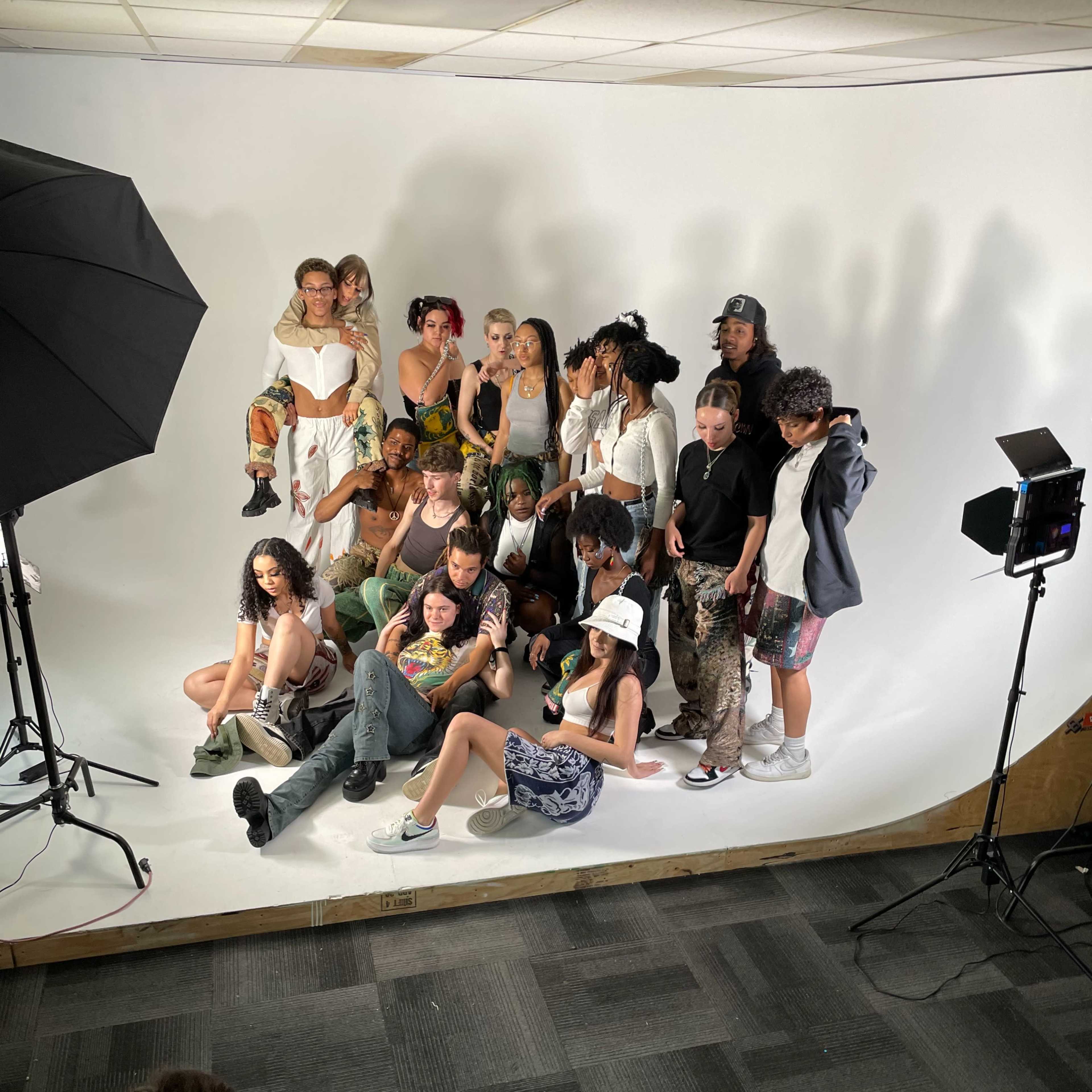 A group of diverse models poses together for a photoshoot in a studio with soft lighting and a plain backdrop.