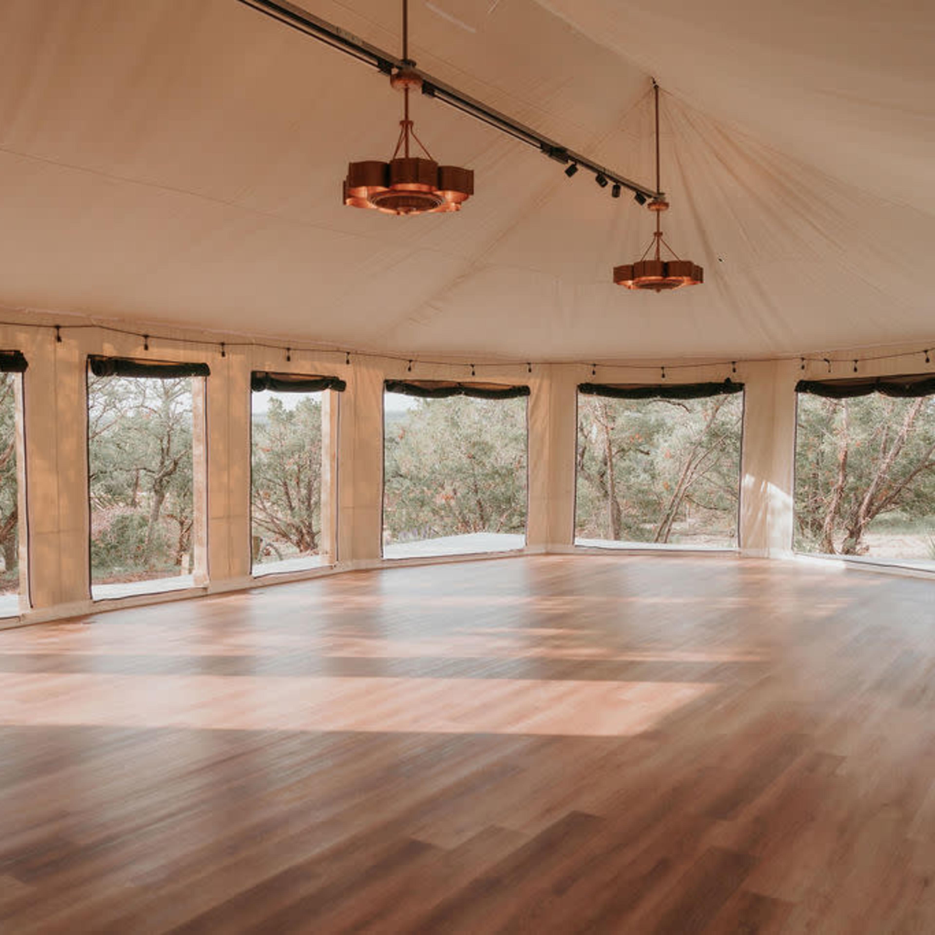 A spacious, illuminated interior of a tent with large windows and wooden flooring.