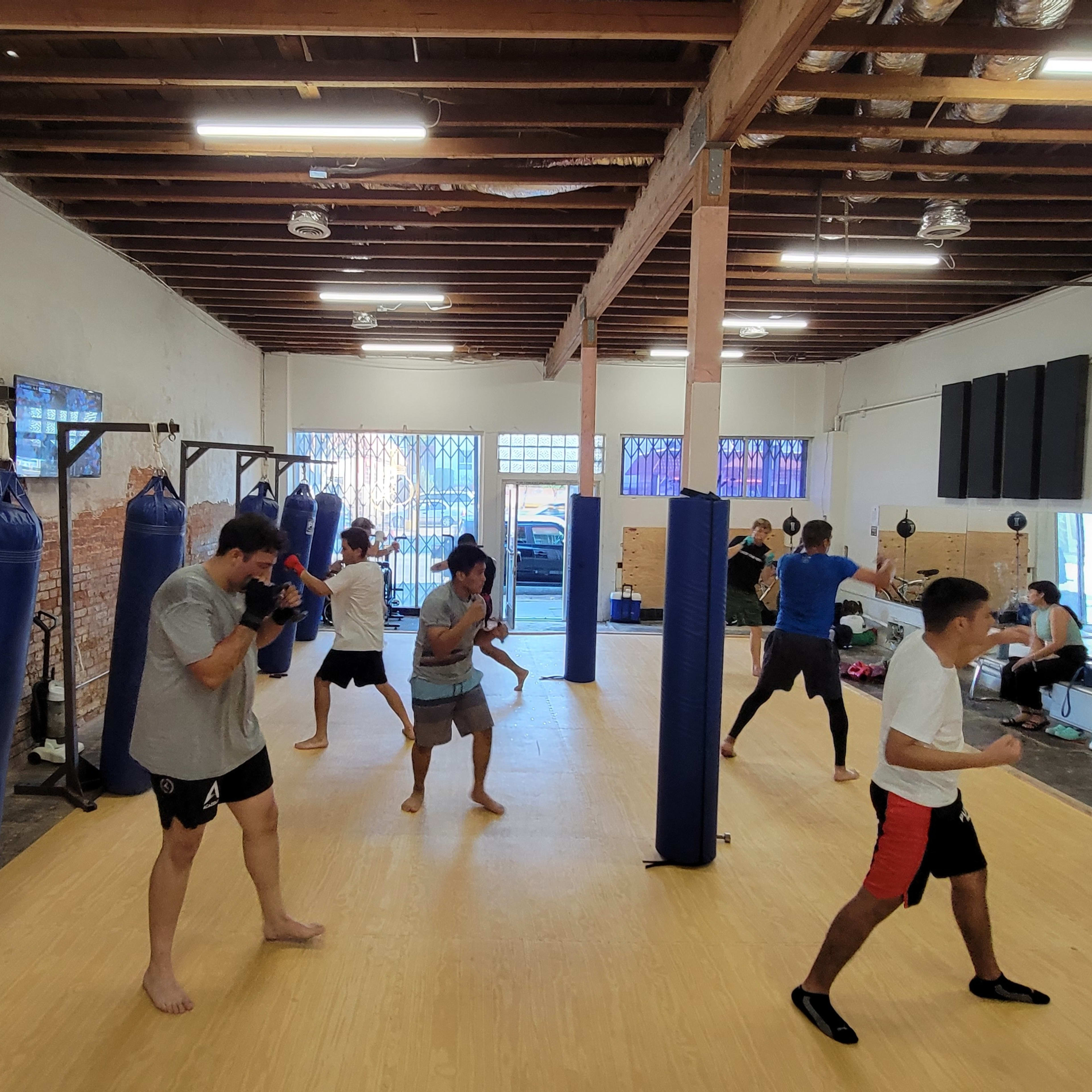A group of individuals trains in a boxing gym with heavy punching bags and a wooden floor.