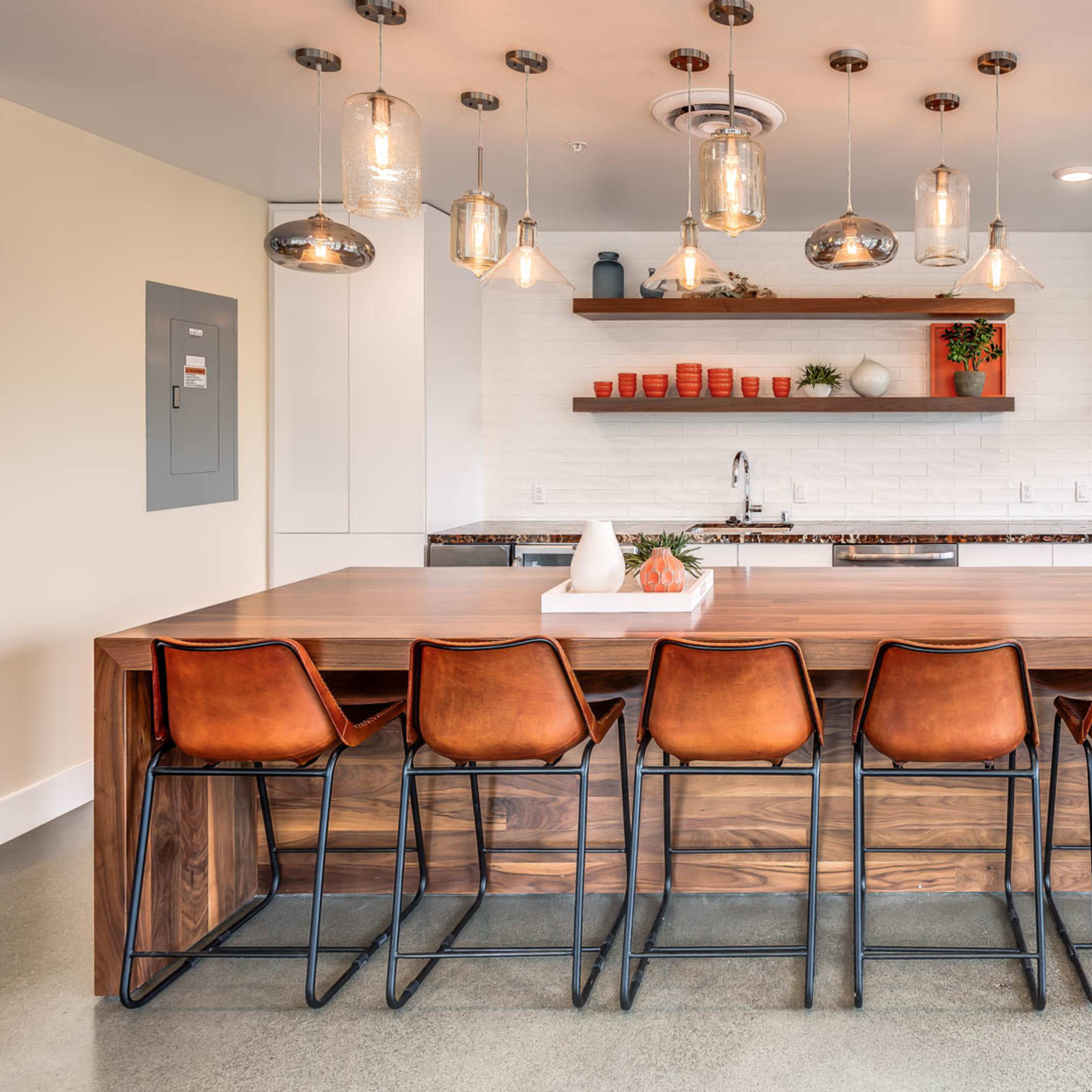 A modern kitchen features a large wooden island with metal bar stools, pendant lighting, and a minimalist design.