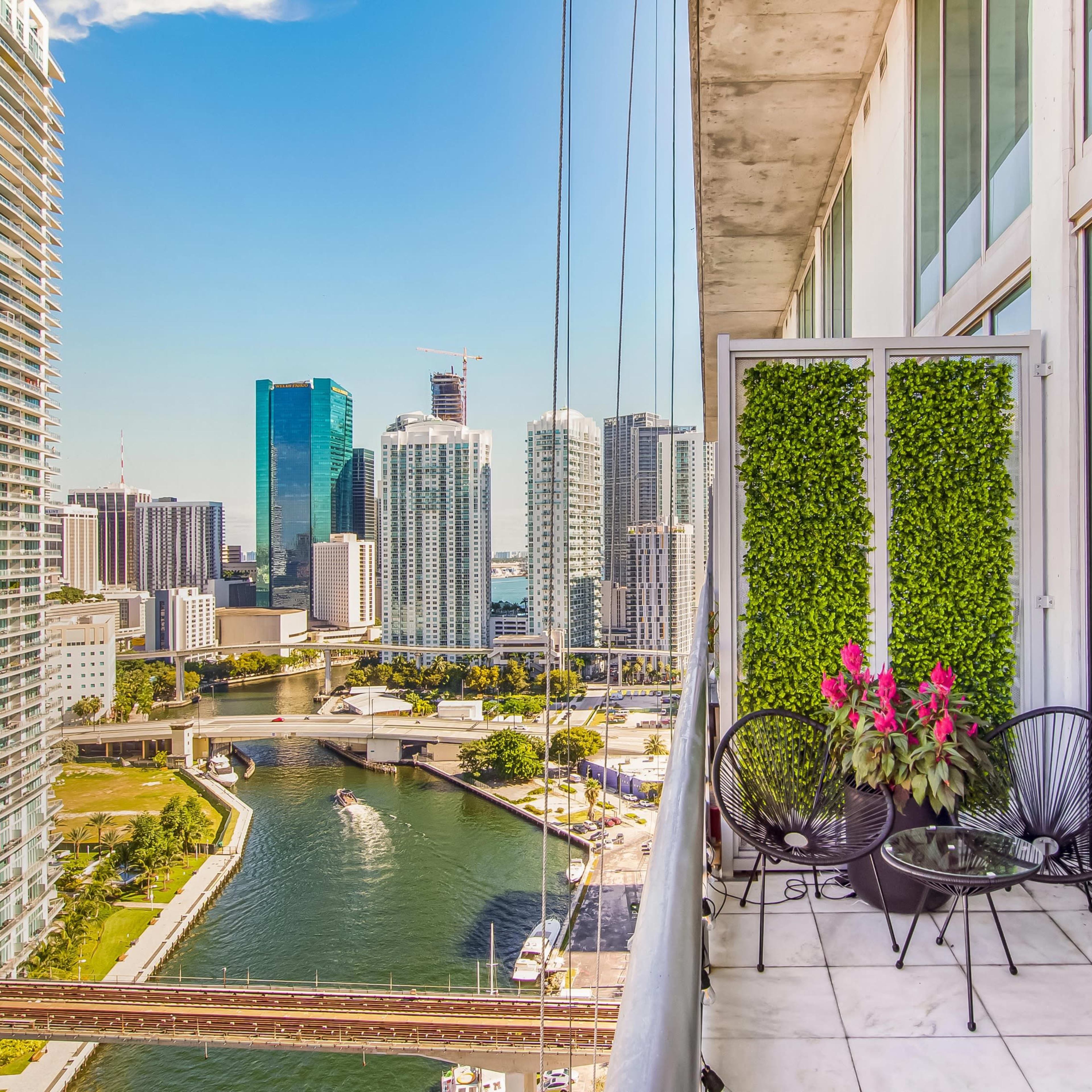 A balcony with potted plants overlooks a river and city skyline featuring modern skyscrapers.