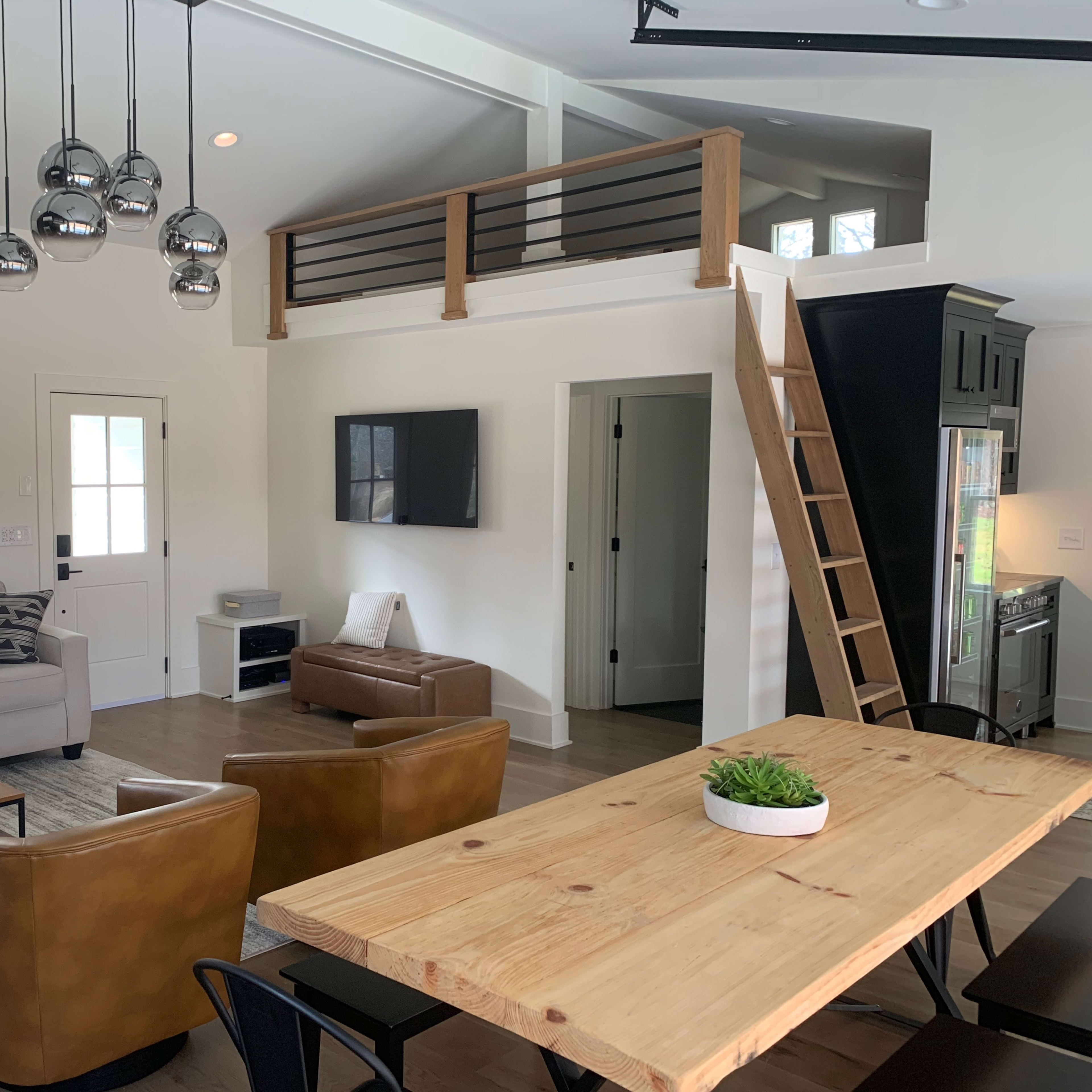 A modern living space with a seating area, a wooden dining table, and a ladder leading to a loft.