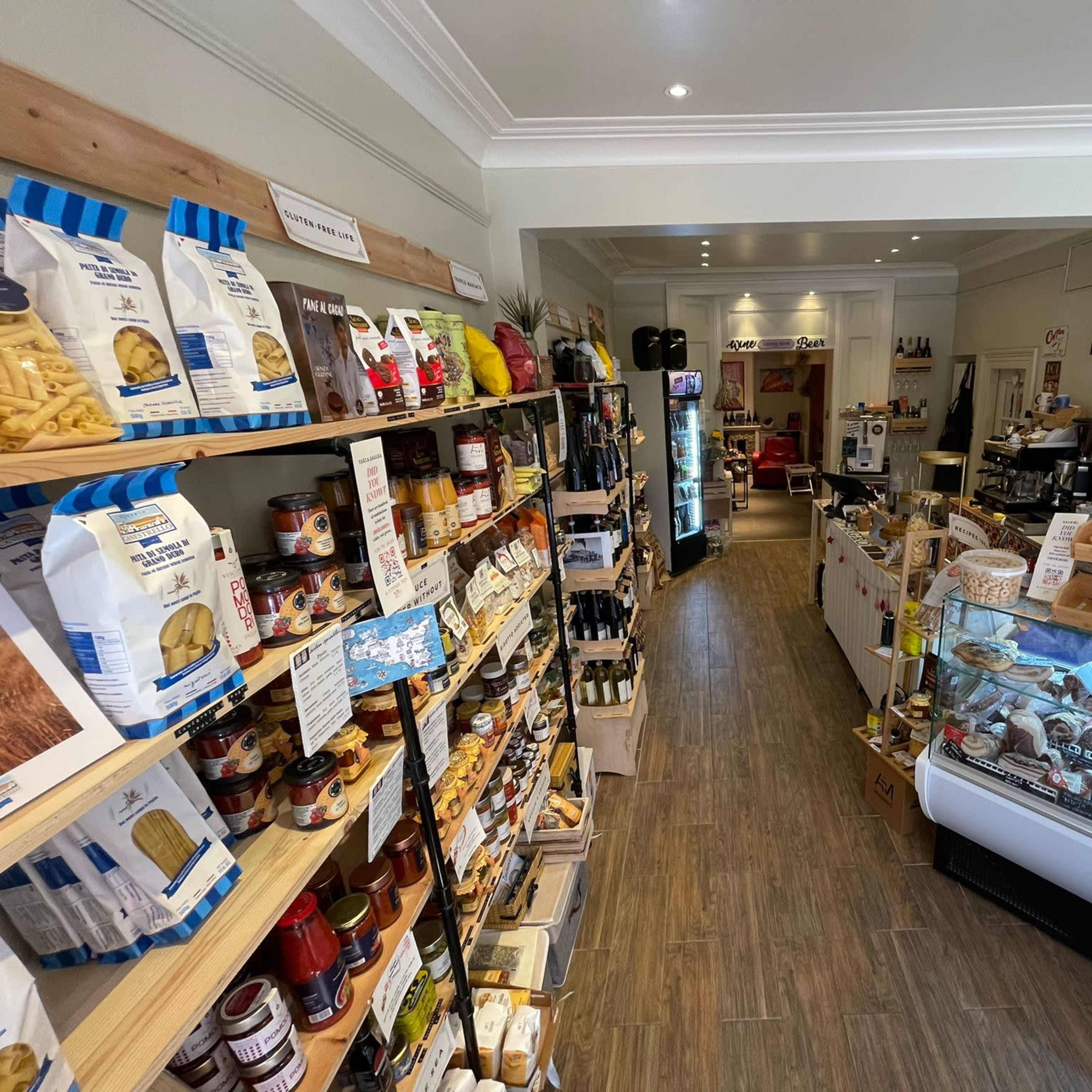 The interior of a small grocery store with shelves stocked with various foods and a deli counter at the back.
