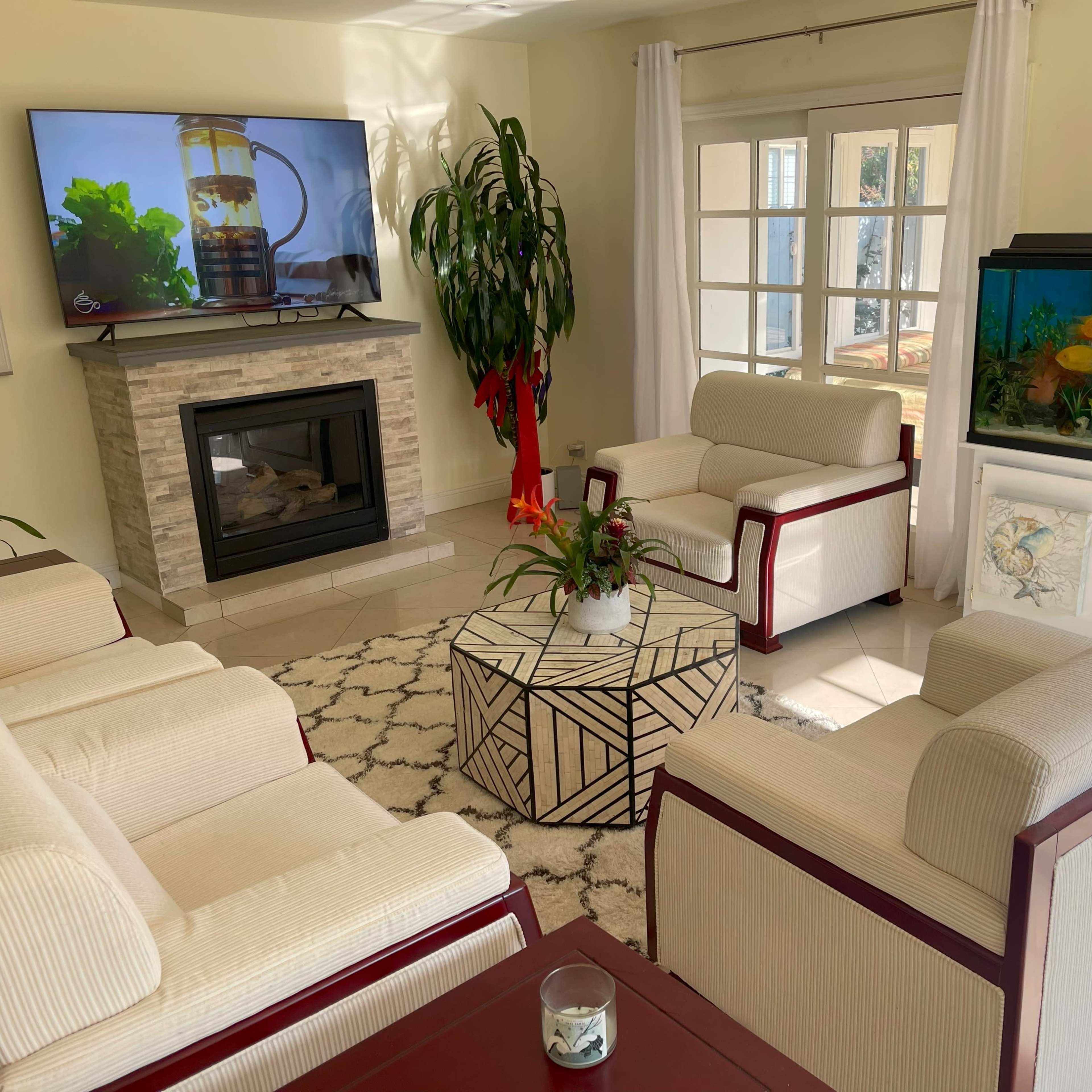 A living room with a fireplace, a large television mounted on the wall, a fish tank, and seating arranged around a geometric coffee table.