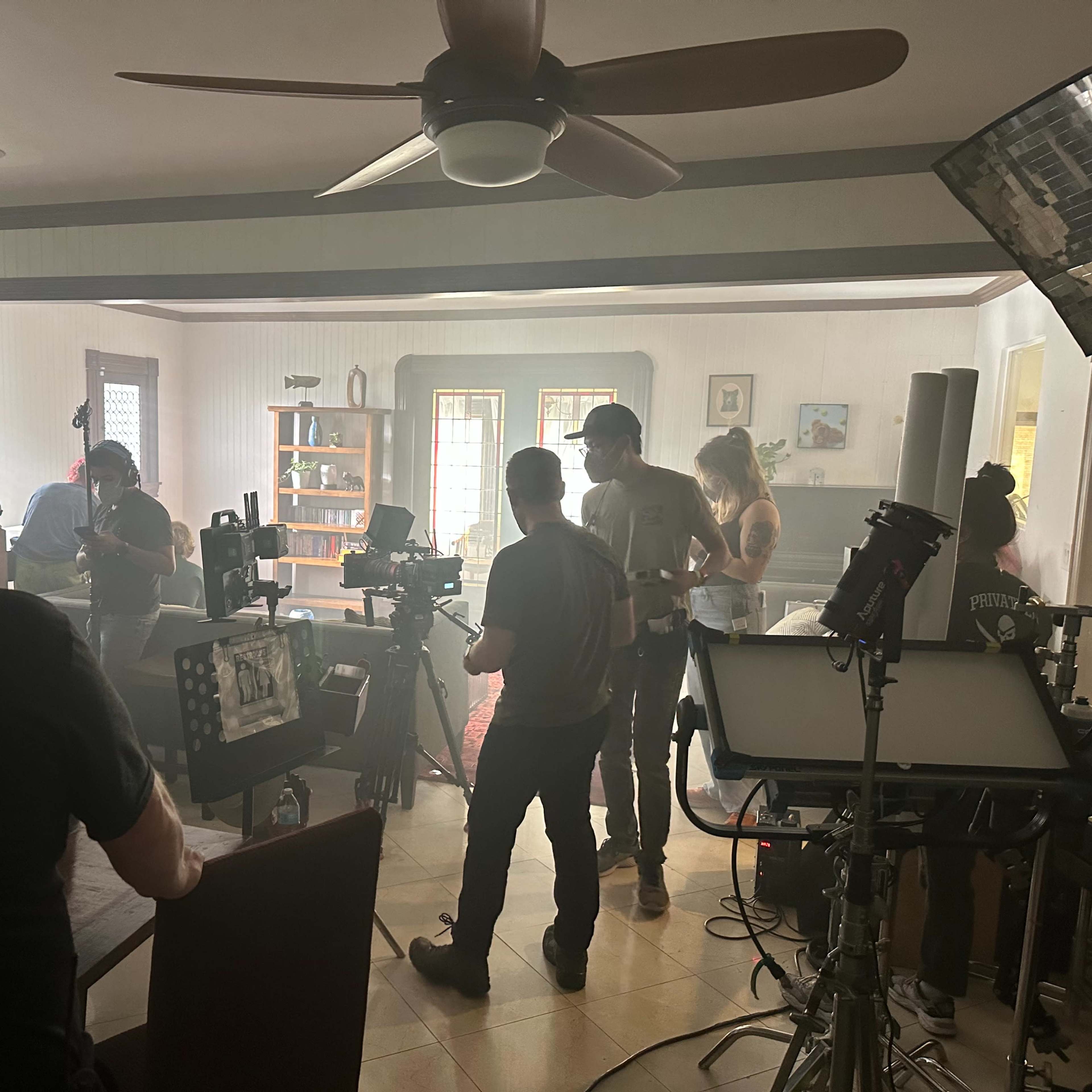 A film crew is set up inside a residential room, with cameras and equipment arranged as they prepare for a shoot.