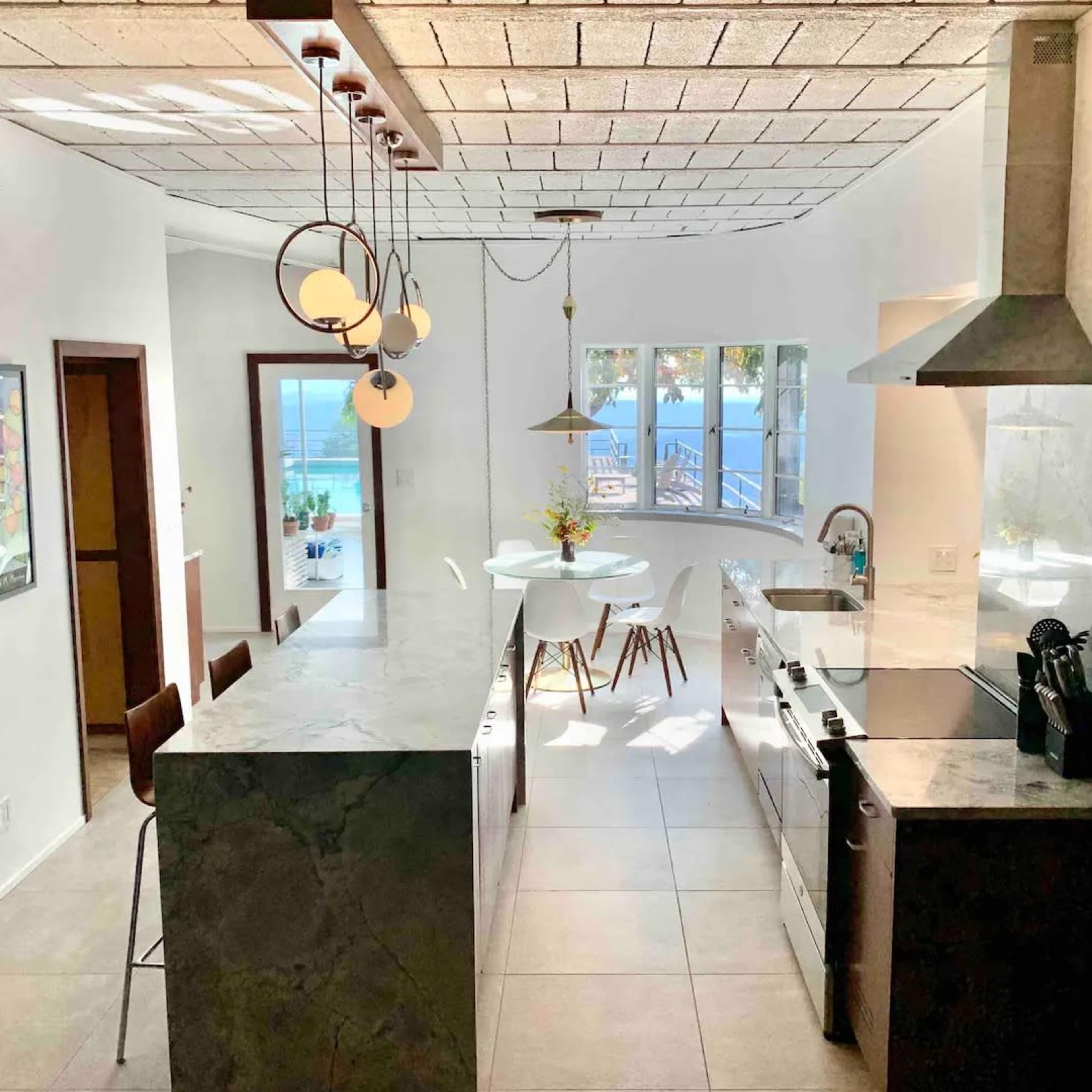 A modern kitchen with a marble island, stainless steel appliances, and a dining area with white chairs and a wooden table.