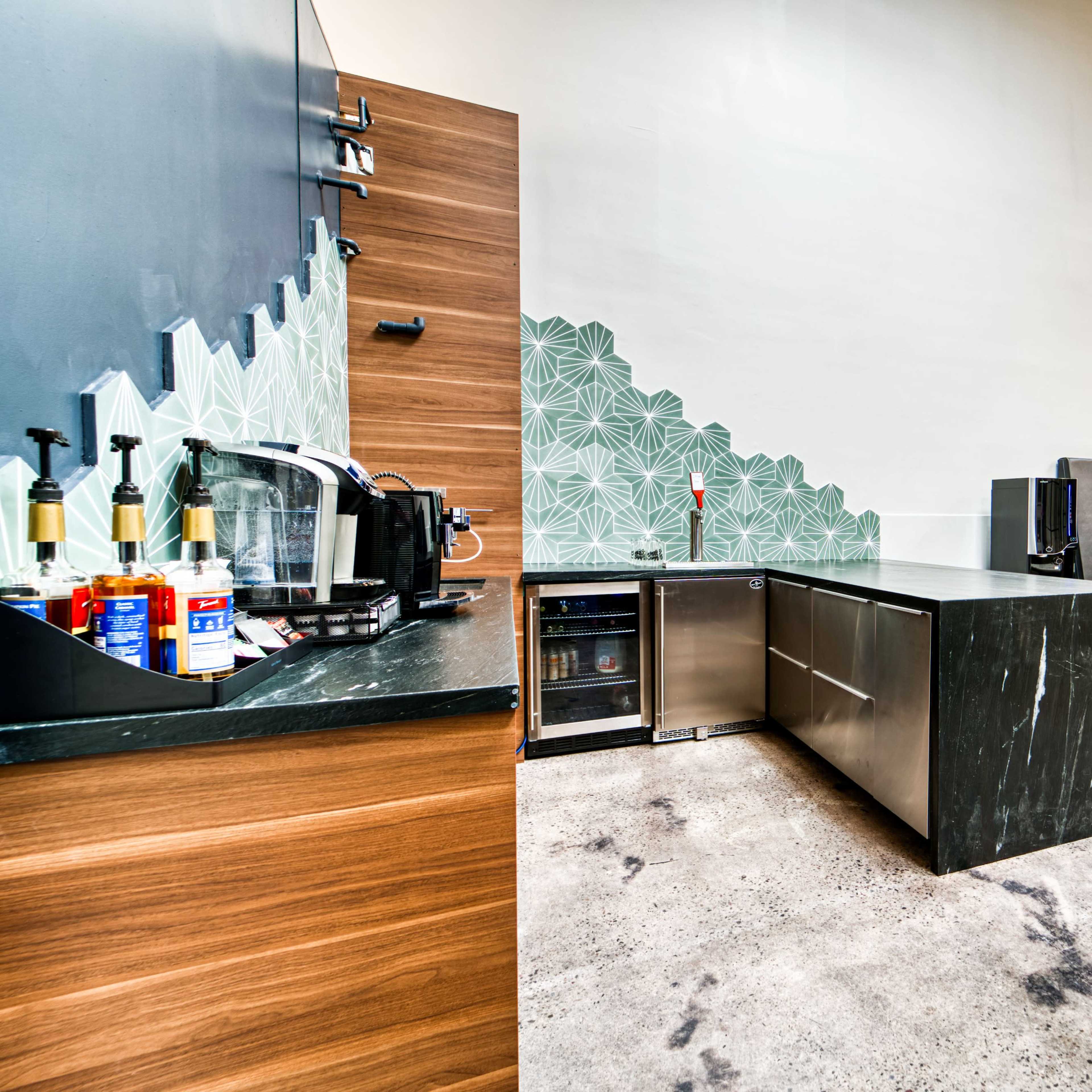 A modern kitchen area with a large island, a coffee station, and seating booths against a decorated wall.