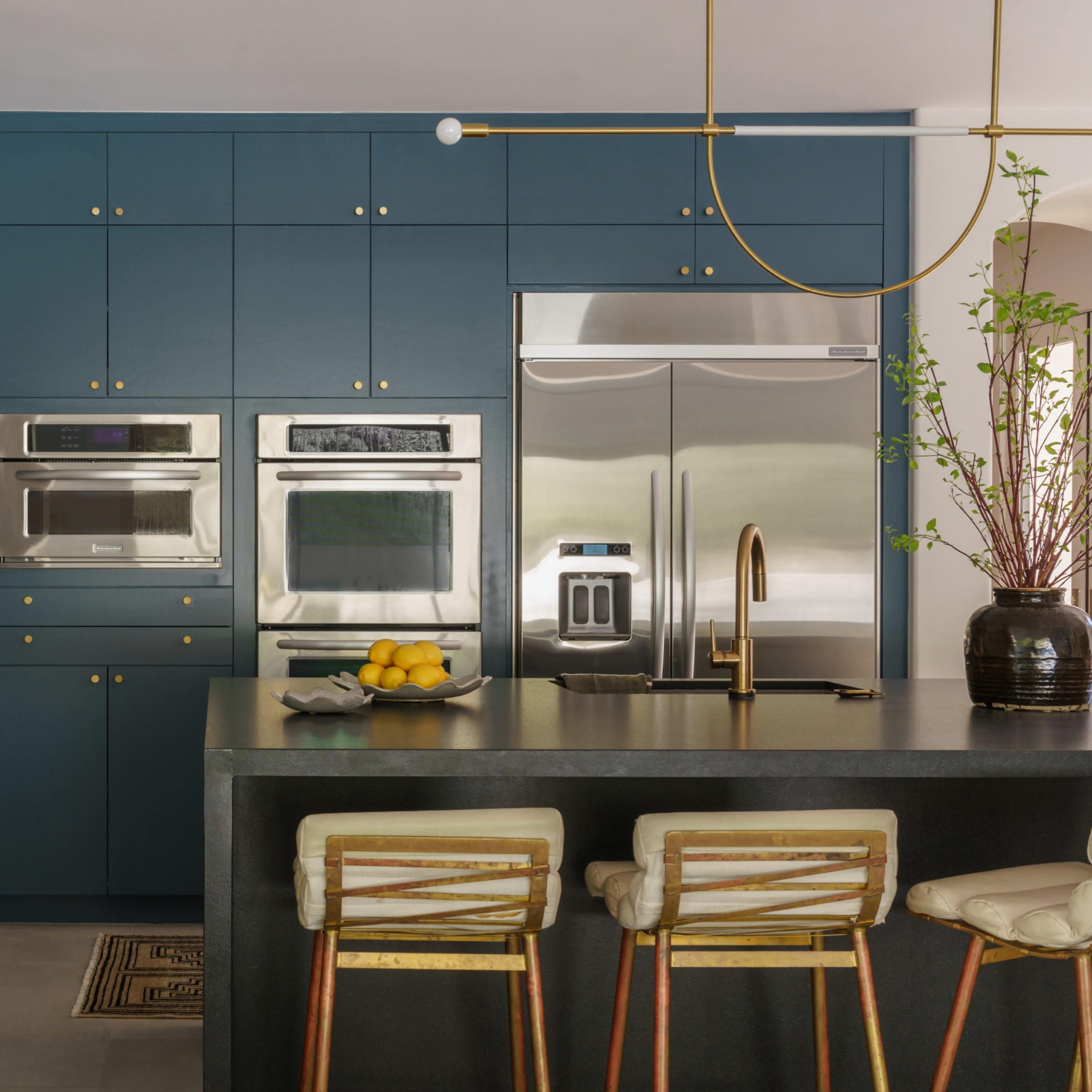 A modern kitchen with dark blue cabinets, stainless steel appliances, and a marble countertop, featuring a sleek island with three bar stools.