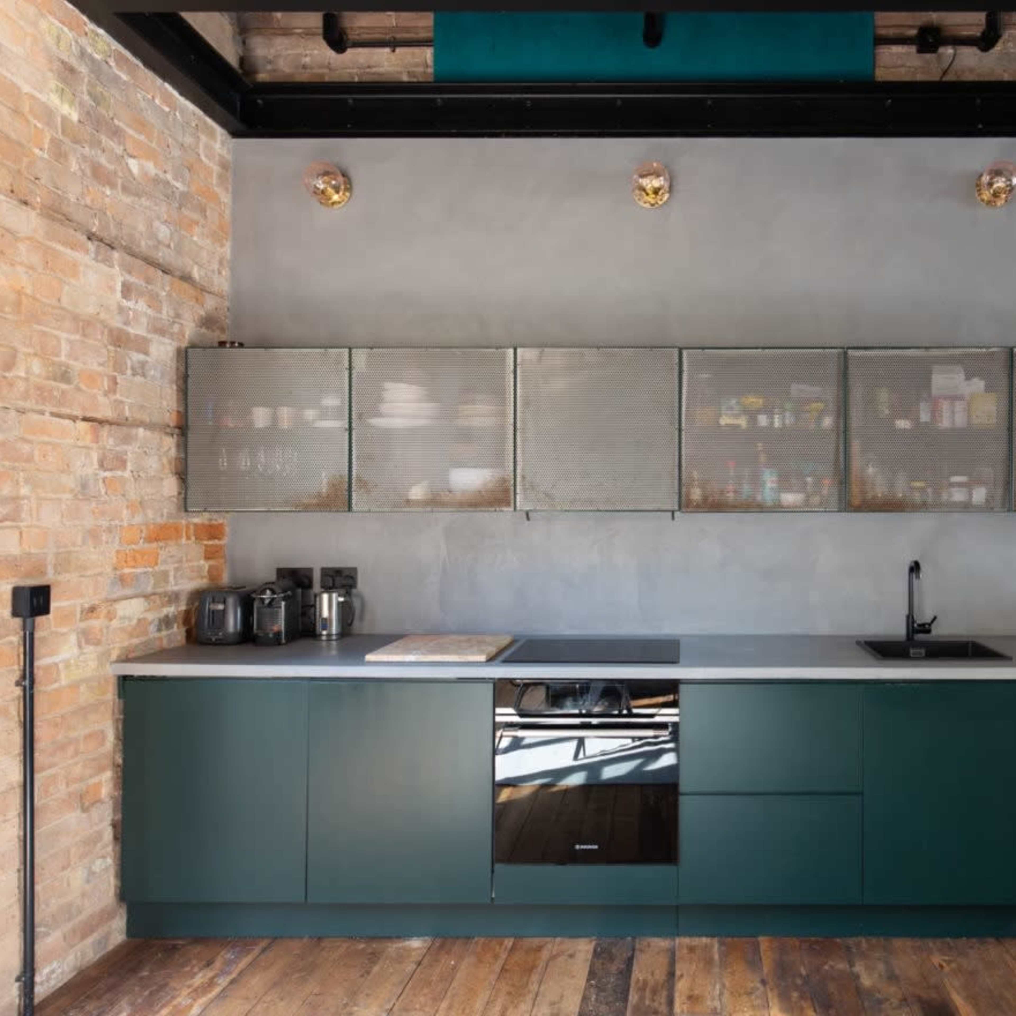 The kitchen features a green cabinetry setup with a gray countertop, wall-mounted metal shelves displaying various dishes, and a modern faucet beneath a window.