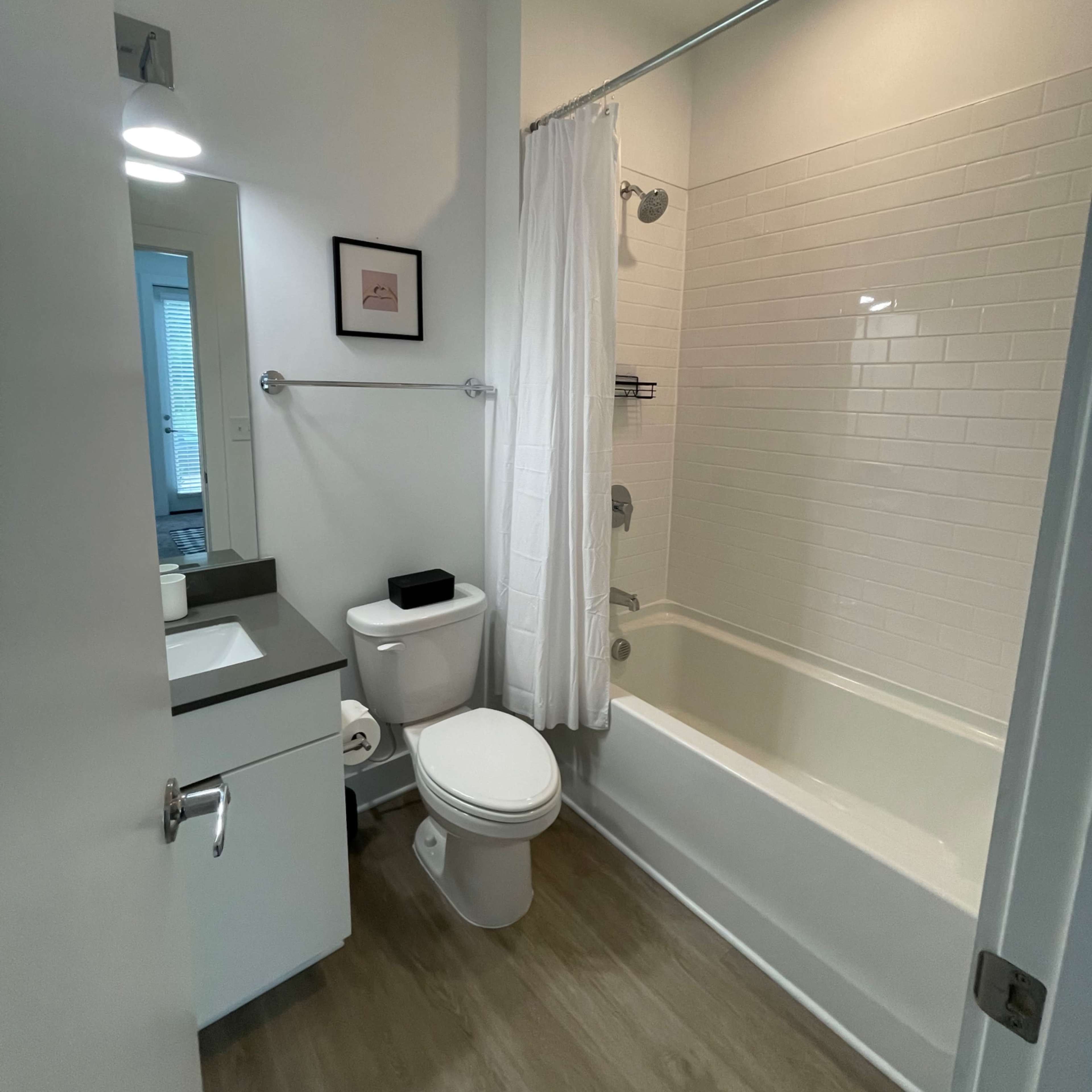 A modern bathroom featuring a bathtub combined with a shower, a toilet, and a sink with a mirror above it.