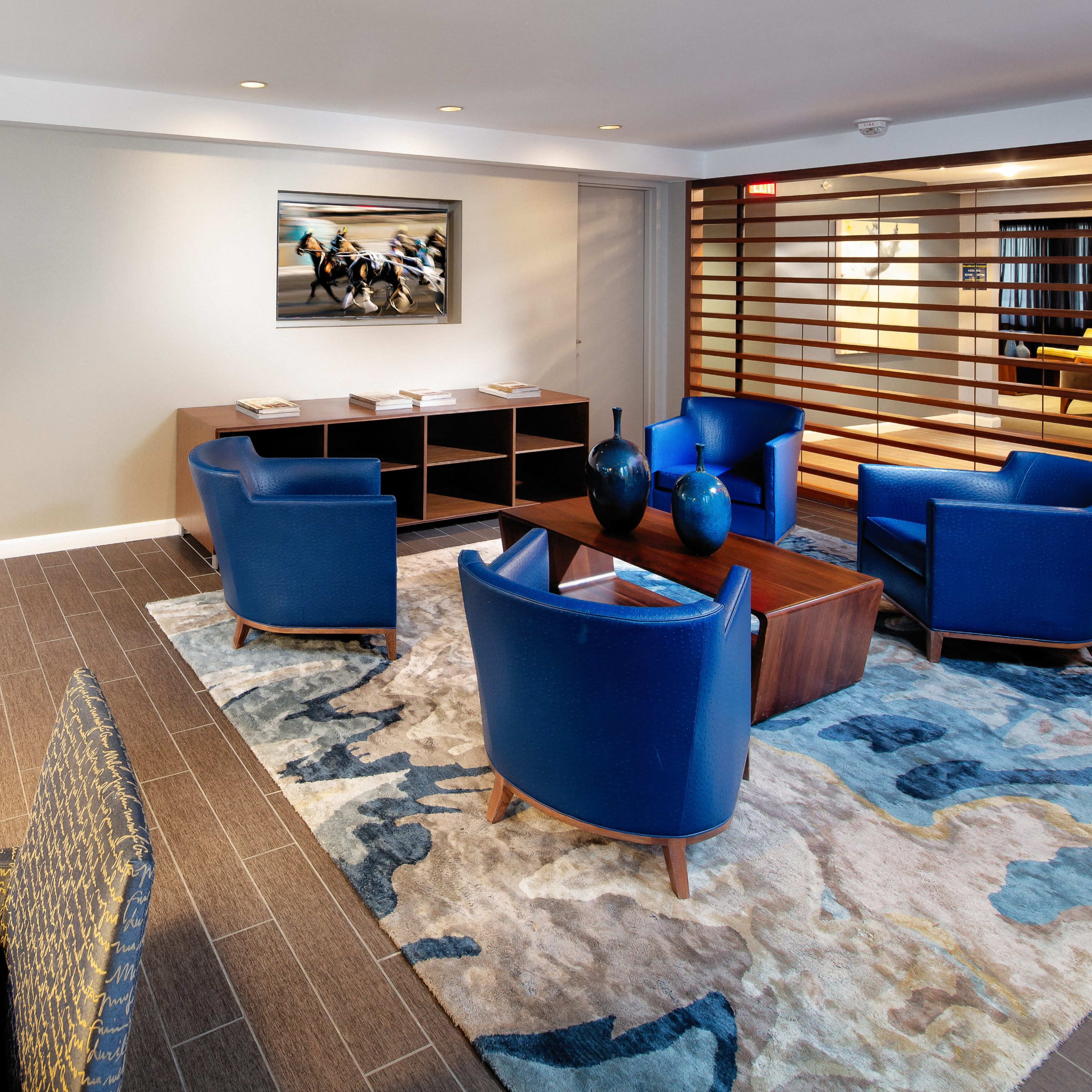 A modern living area with blue chairs, a wooden coffee table, a patterned rug, and a kitchen area in the background featuring a sleek design.