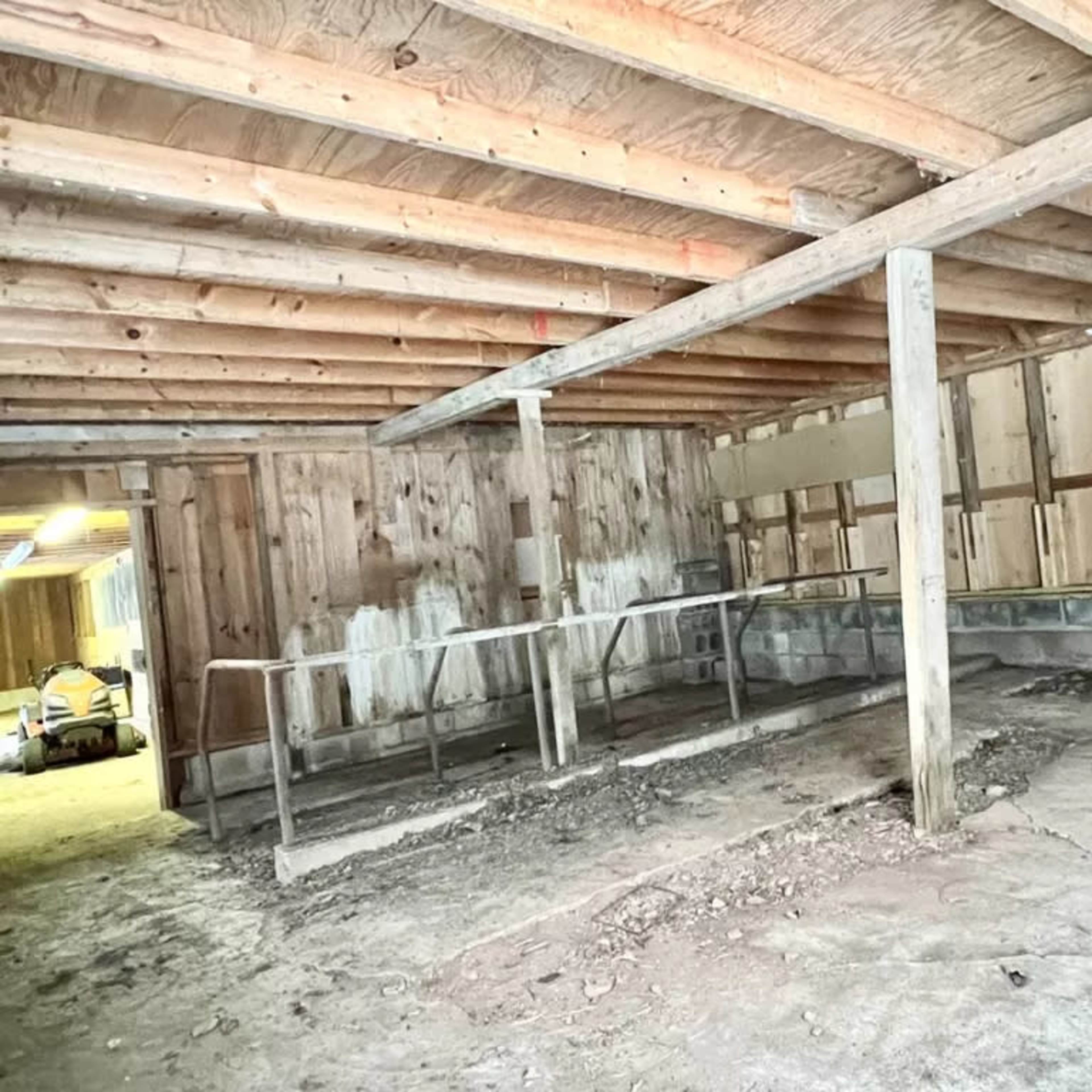 An empty, unfinished interior space with exposed wooden beams and a concrete floor, featuring a metal railing along one wall.