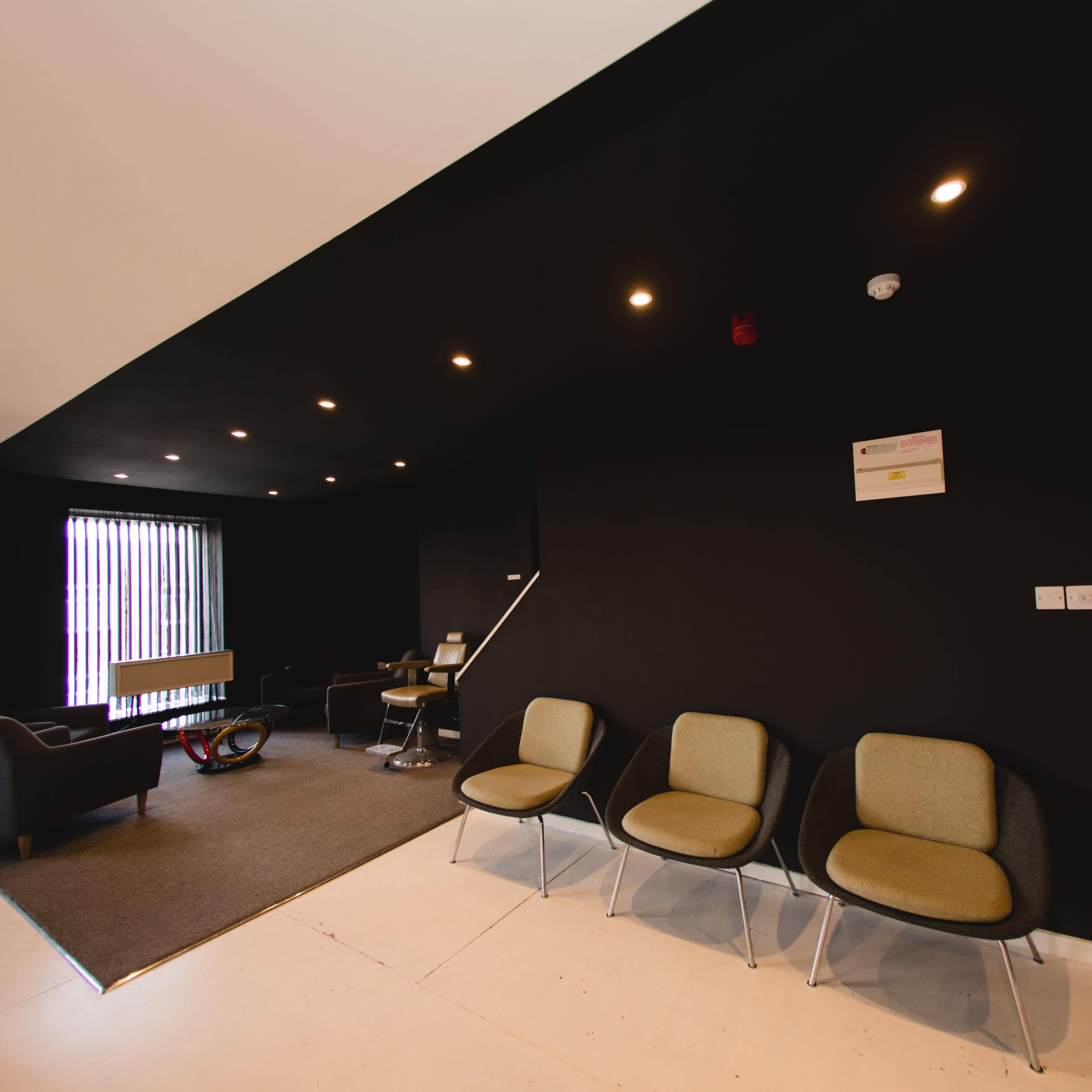A modern interior space with a black wall, three gray chairs, and a small table in a lounge area.