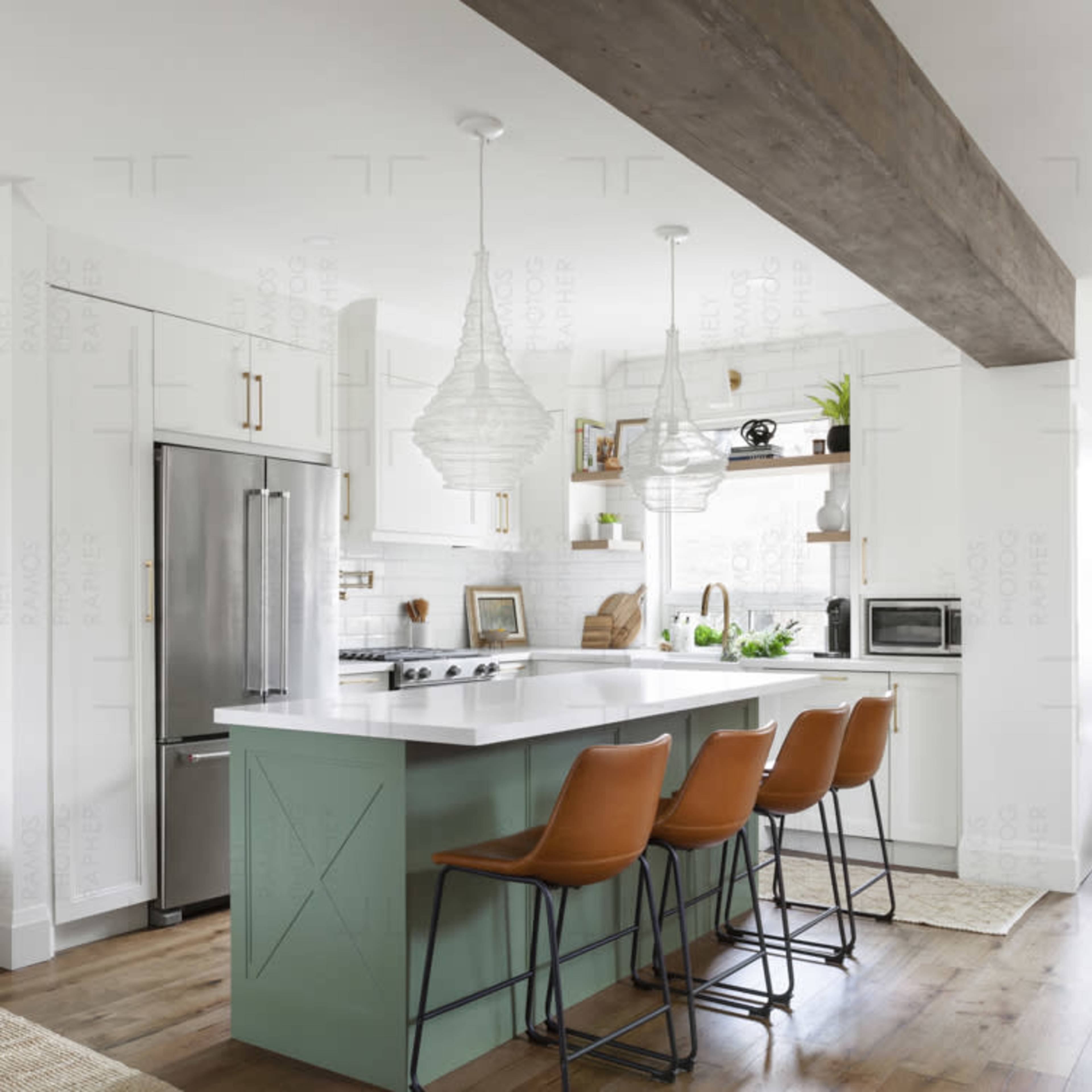A modern kitchen features a large island with green cabinetry and three brown bar stools, flanked by pendant lights and stainless steel appliances.