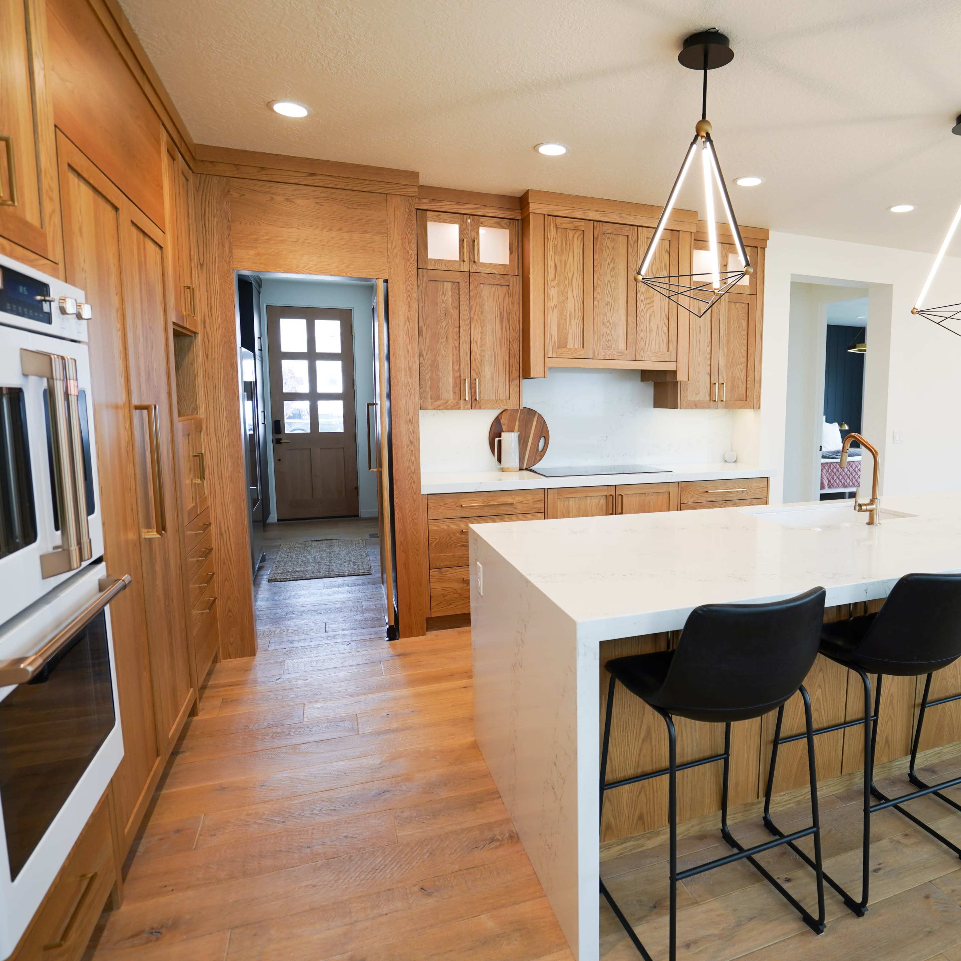 A modern kitchen with wood cabinetry, an island featuring bar stools, and bright pendant lighting.